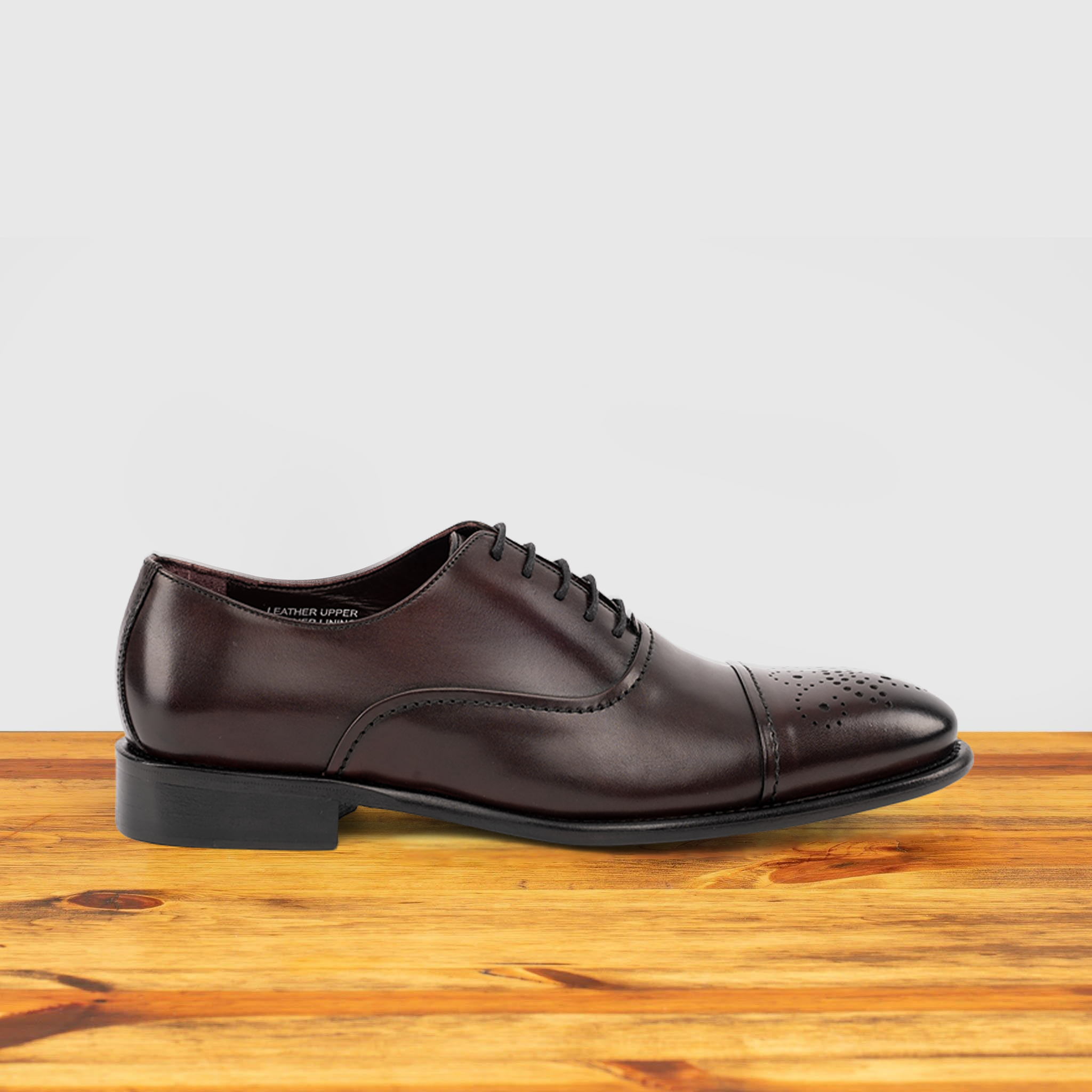 Burgundy leather dress shoe on a wooden surface with a white background