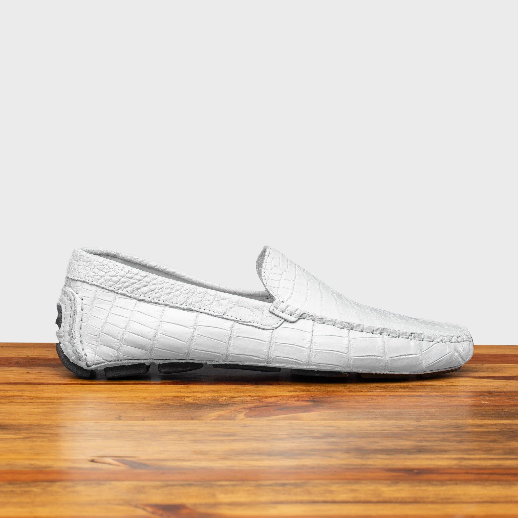 White crocodile-patterned loafer on a wooden surface with a light gray background