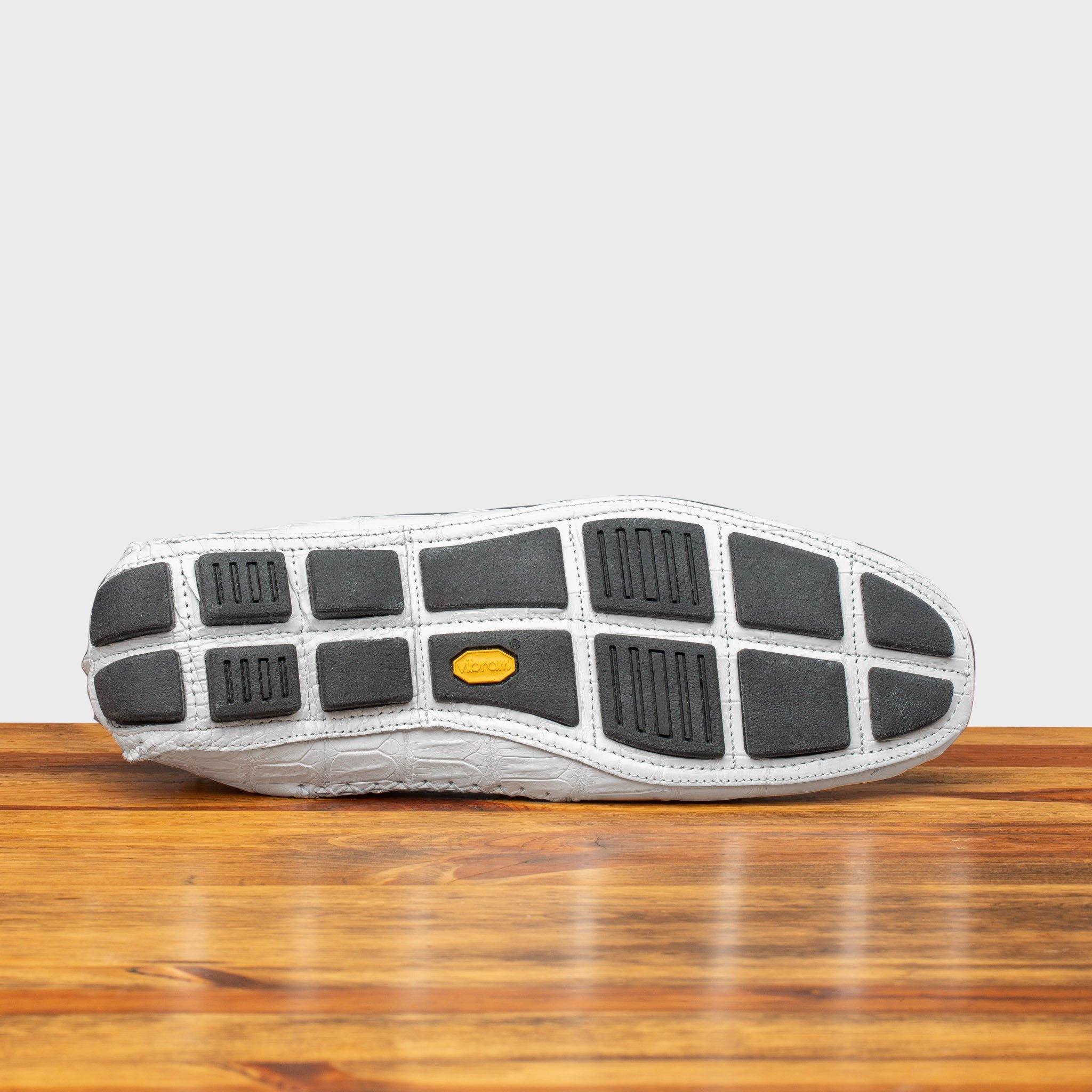 Outsole of White crocodile-patterned loafer on a wooden surface with a light gray background