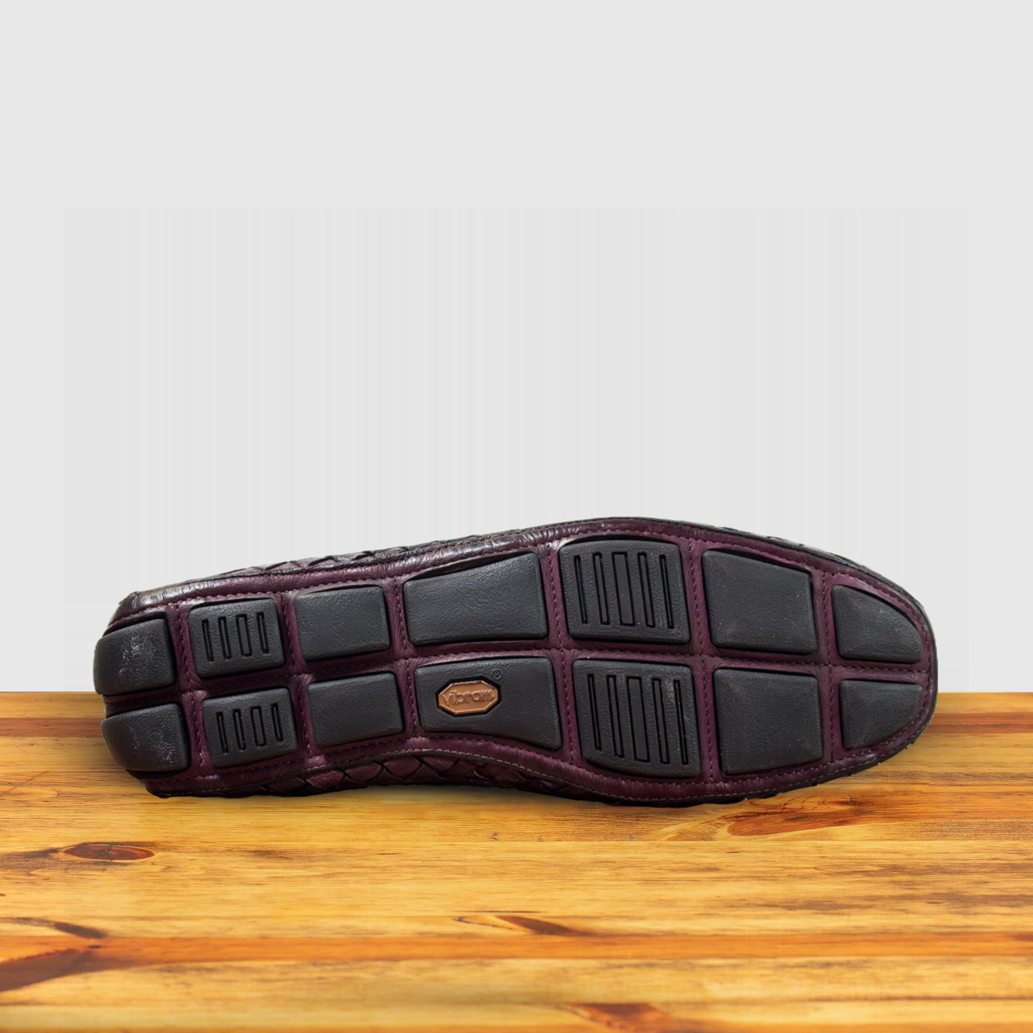 Outsole of Merlot loafer shoe with woven pattern on a wooden surface