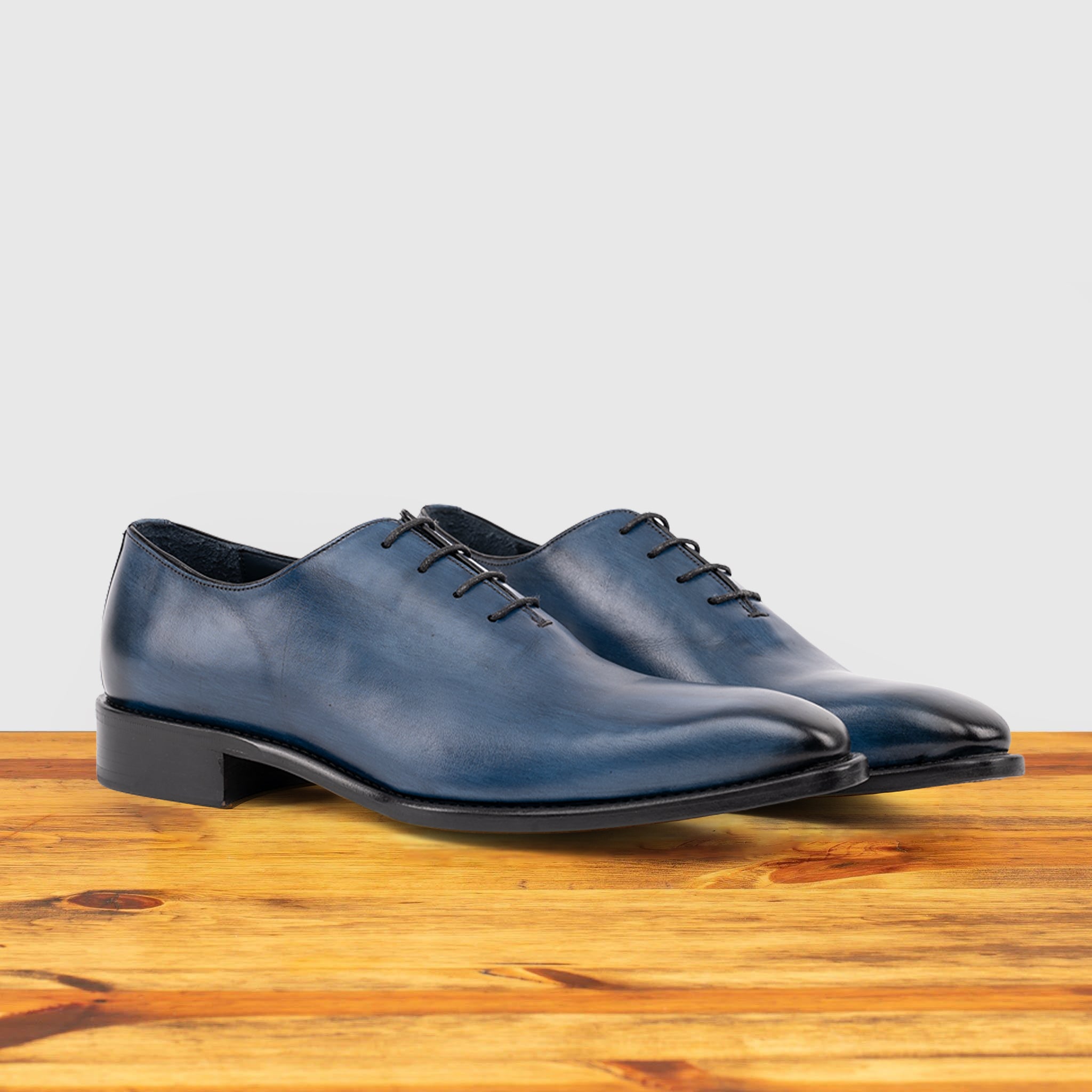 Pair of Blue leather dress shoe on a wooden surface with a light gray background