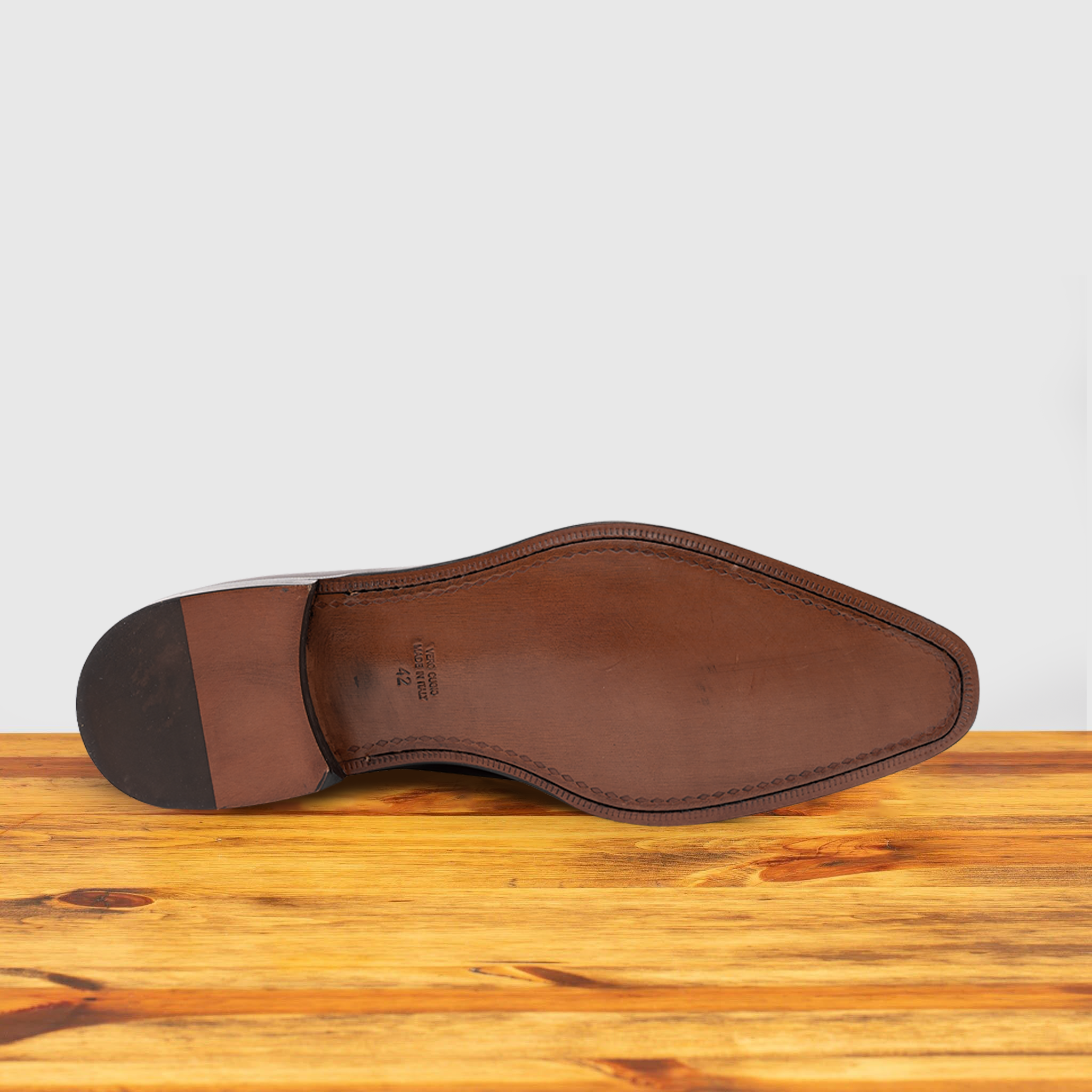 Outsole of Blue leather dress shoe on a wooden surface with a light gray background