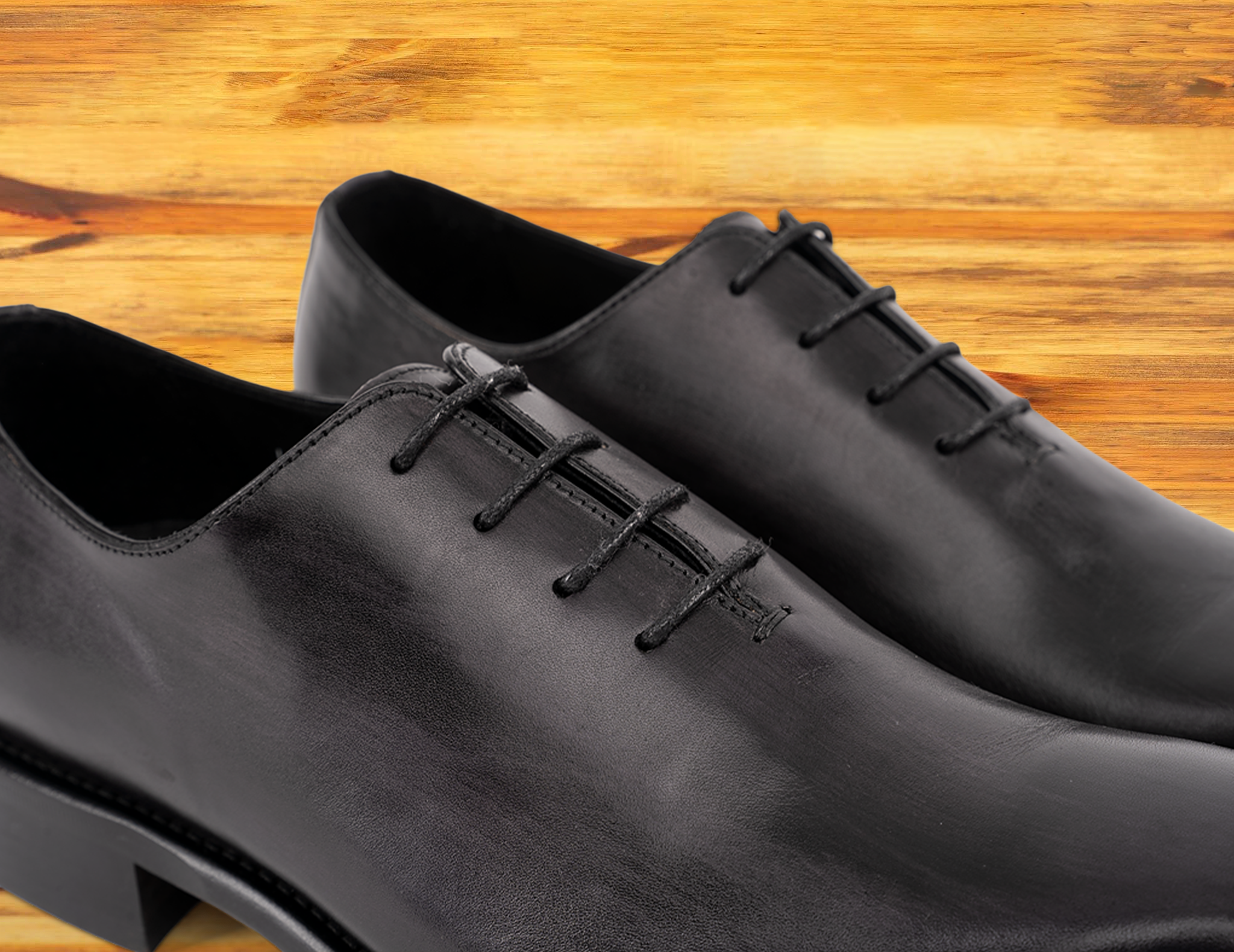 A Pair of Graphite Italian wholecut Oxford shoe with laces on a wooden surface.