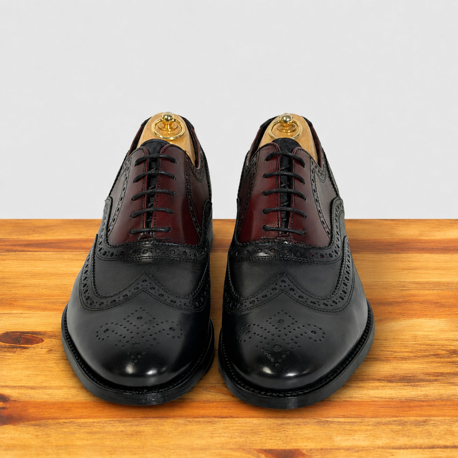 A pair of men's blue leather wingtip brogue shoes with dark burgundy vamps, displayed on a wooden surface against a light gray background.