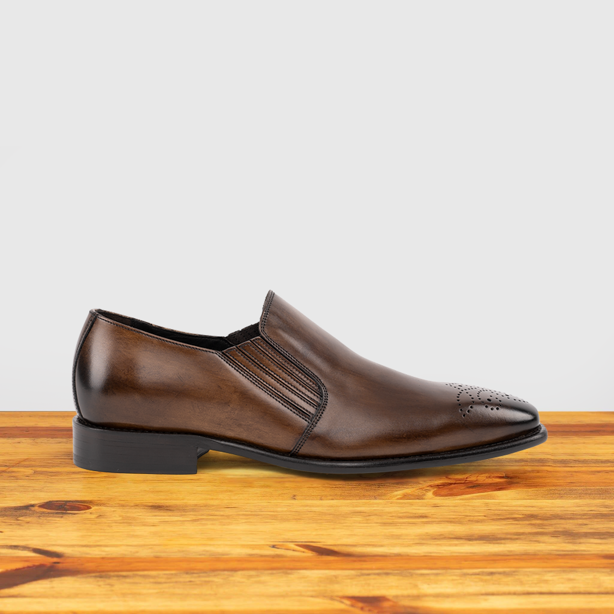 Brown leather shoe on a wooden surface with a light gray background