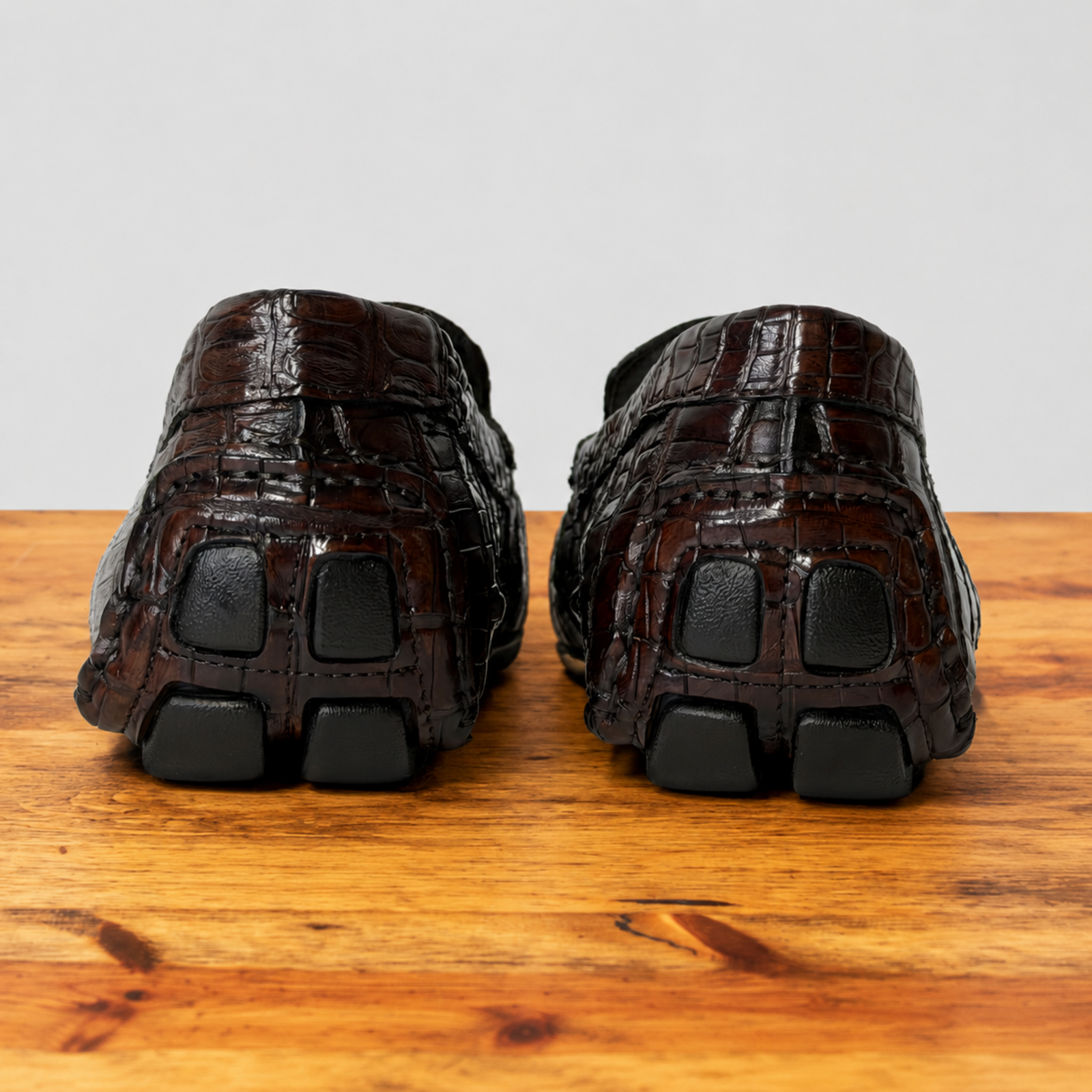 A pair of cerris color crocodile-shoes shown from the back, resting on a wooden surface against a light gray background.