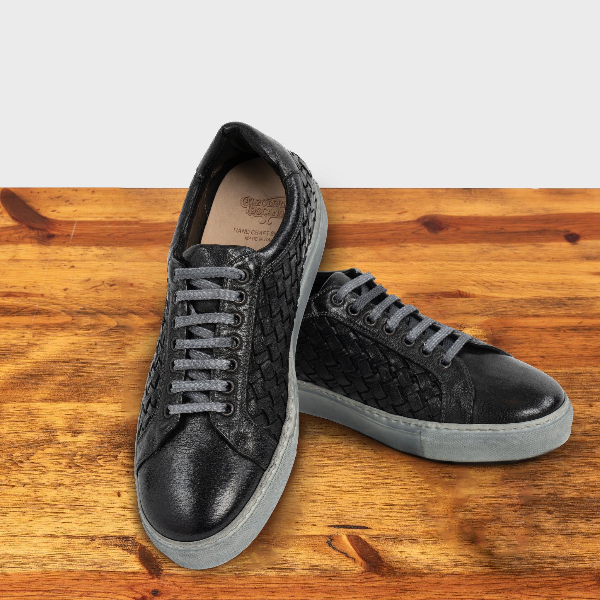 A Pair of Black woven sneaker on a wooden surface with a light gray background