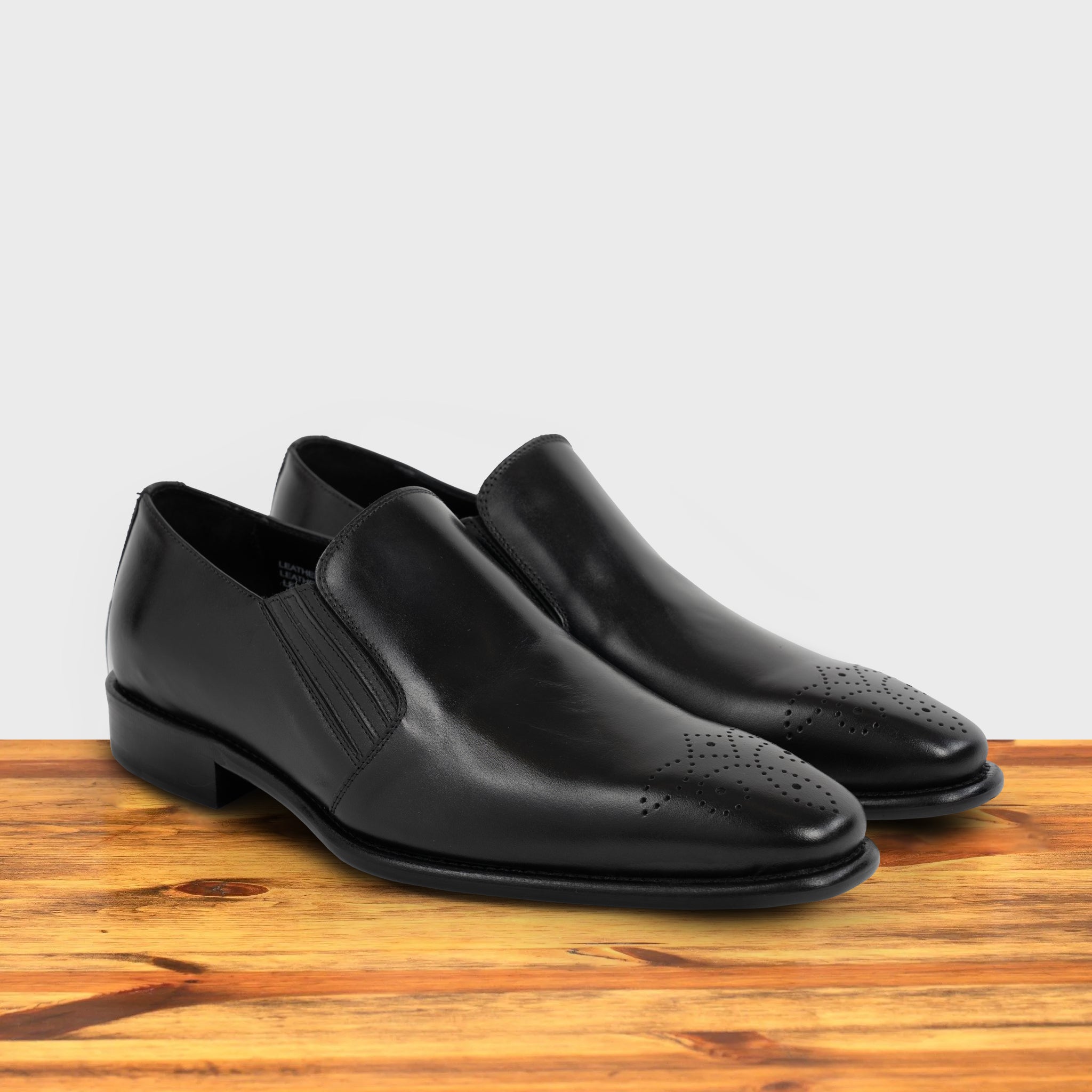 Pair of Black leather shoe on a wooden surface with a light gray background