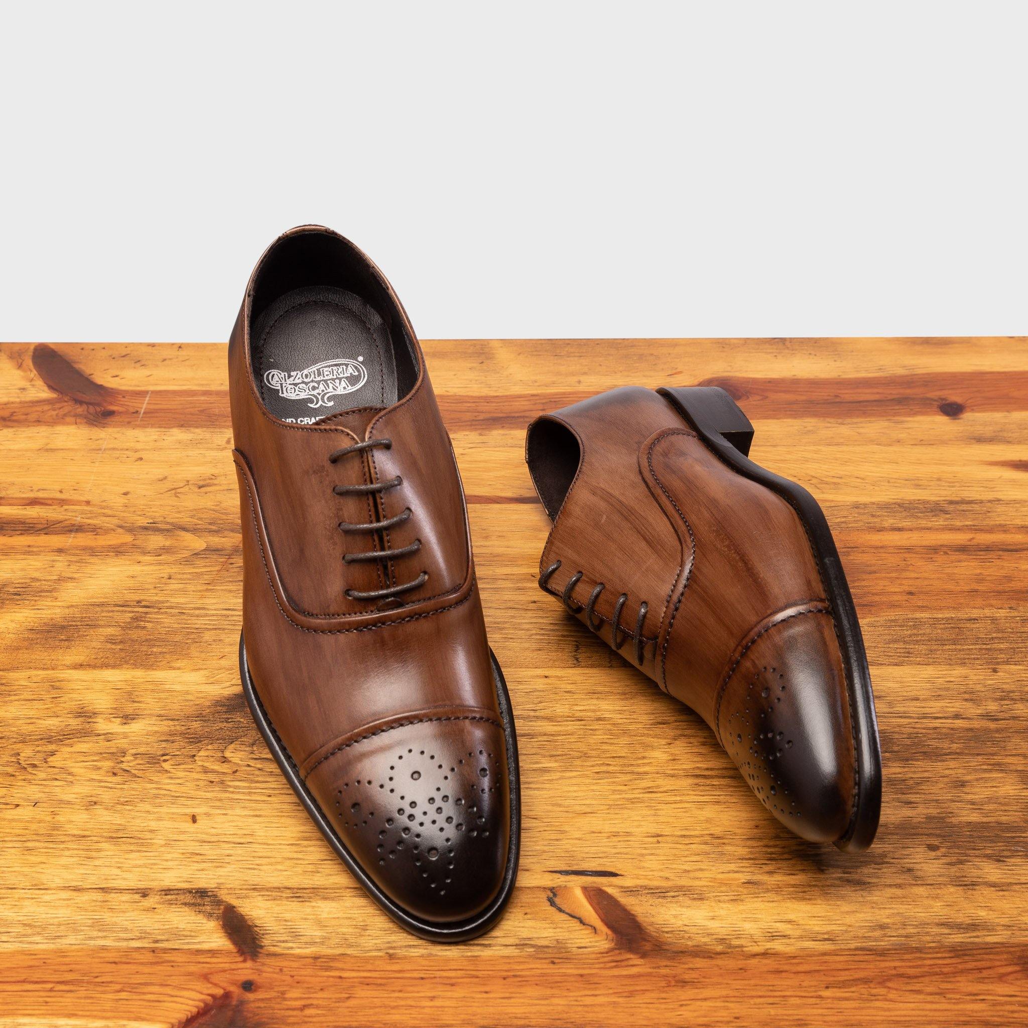 Pair of brown leather oxford dress shoes with a polished finish, on a wooden surface