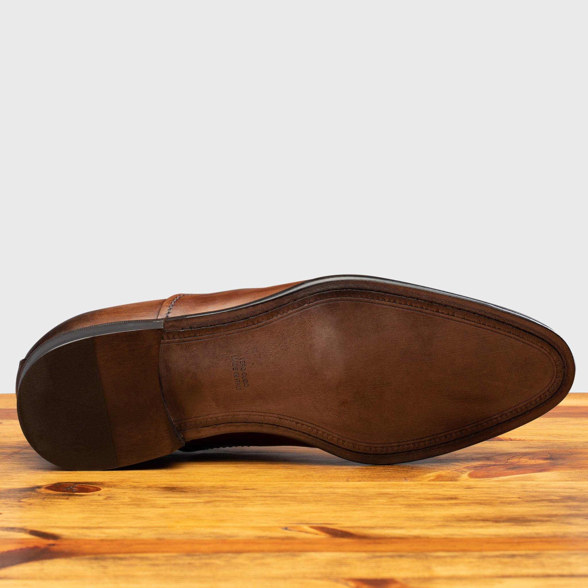 Outsole of Brown leather oxford dress shoe with a cap toe on a wooden surface.