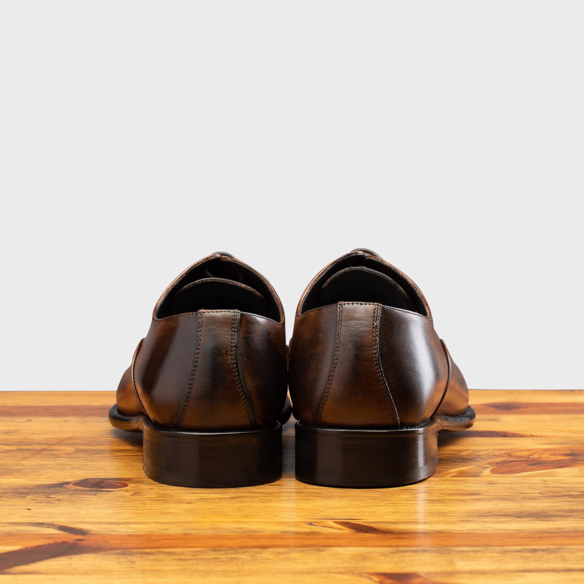 Rear view of a pair of brown leather oxford dress shoes with a polished finish, placed side by side on a wooden surface.