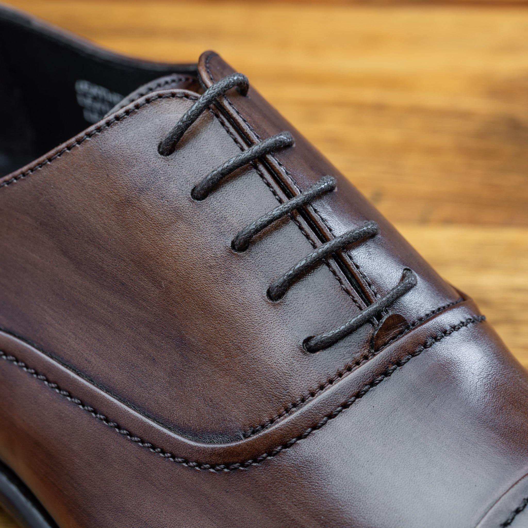 Close view of brown leather oxford dress shoes with a polished finish, on a wooden surface