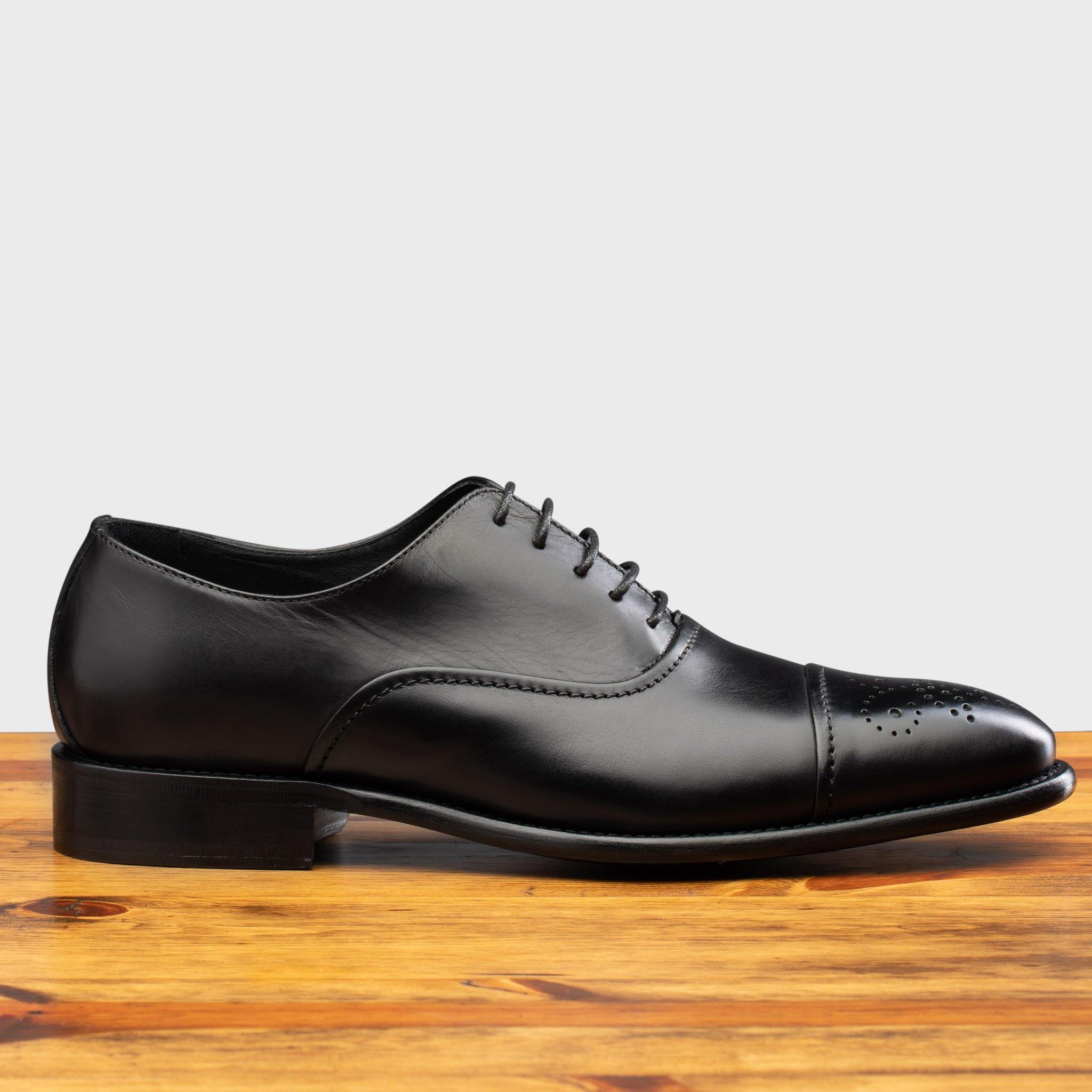Black leather dress shoe on a wooden surface with a white background