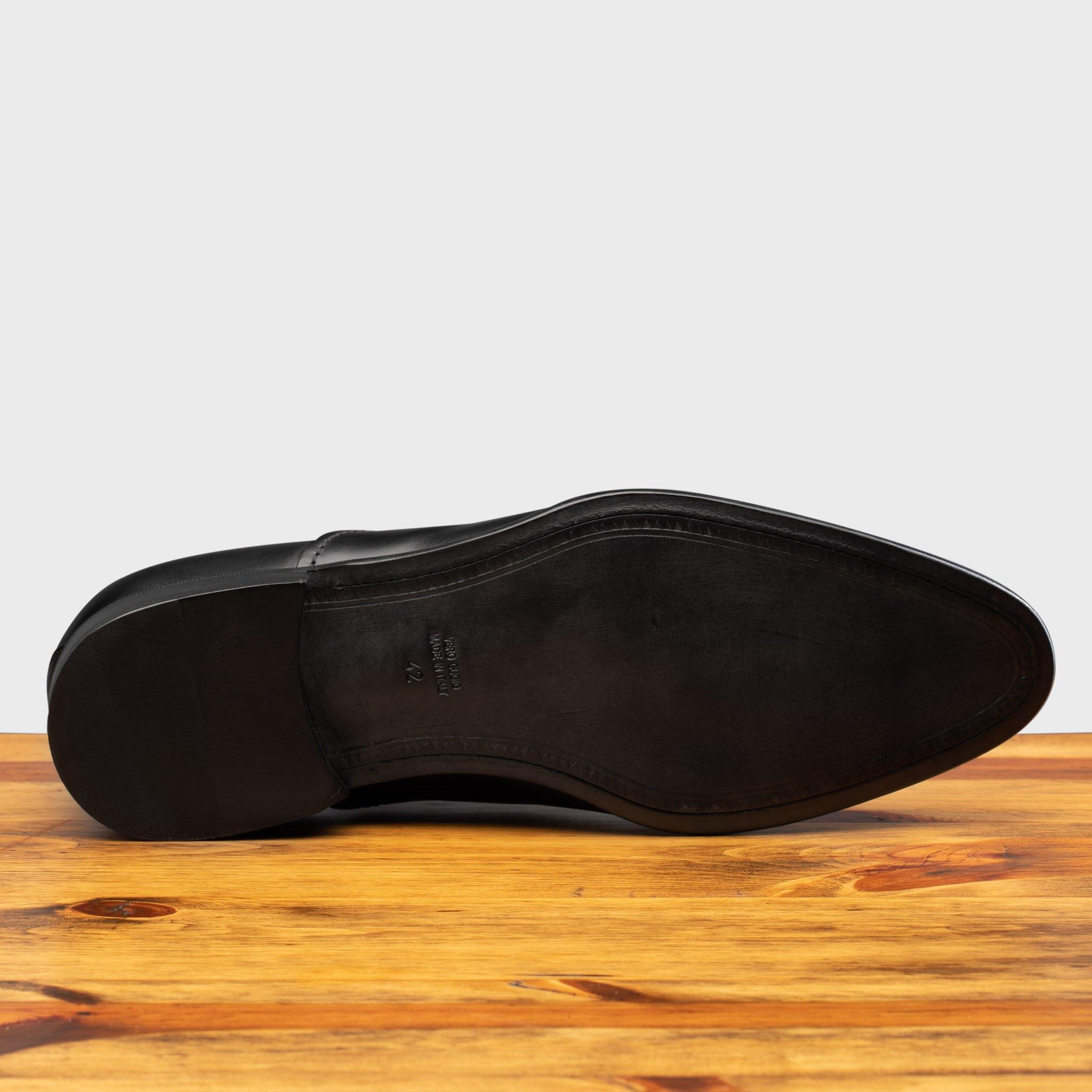 Outsole of Black leather dress shoe on a wooden surface with a white background