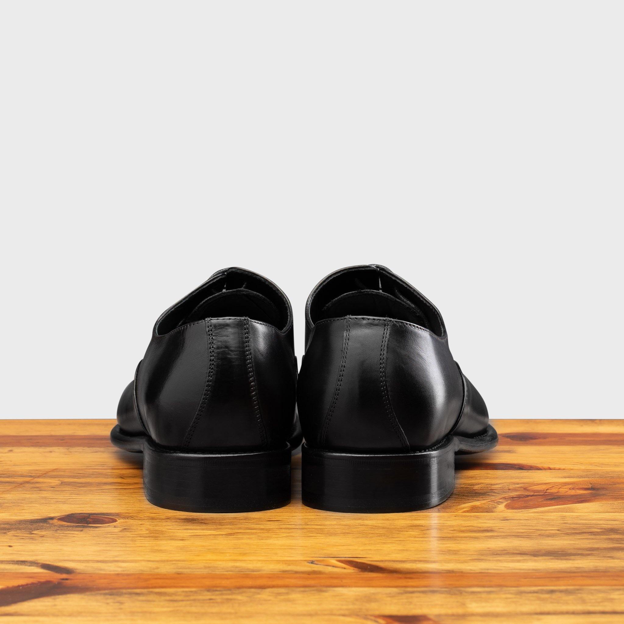 Back view of Black leather dress shoe on a wooden surface with a white background