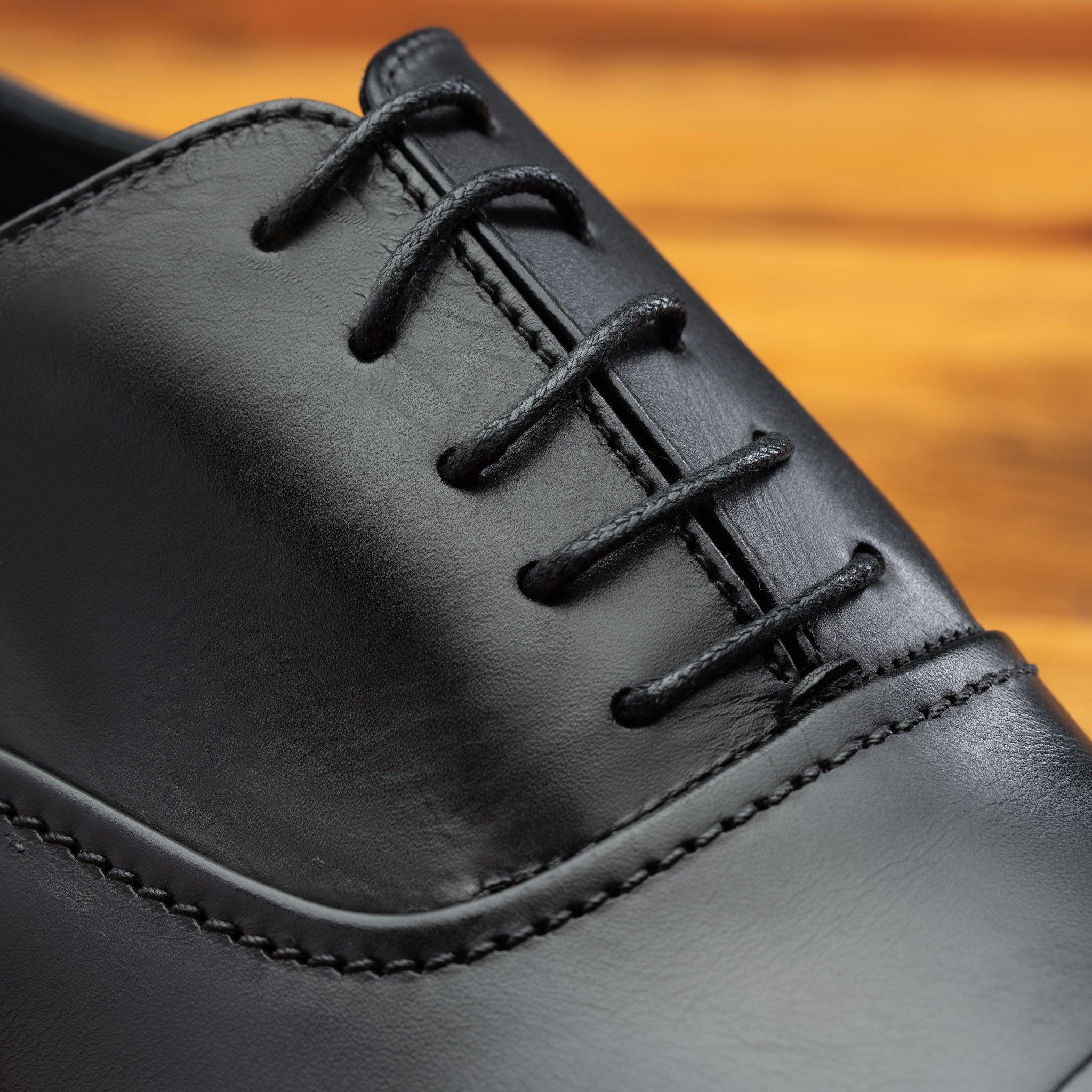 Close view of Black leather dress shoe on a wooden surface