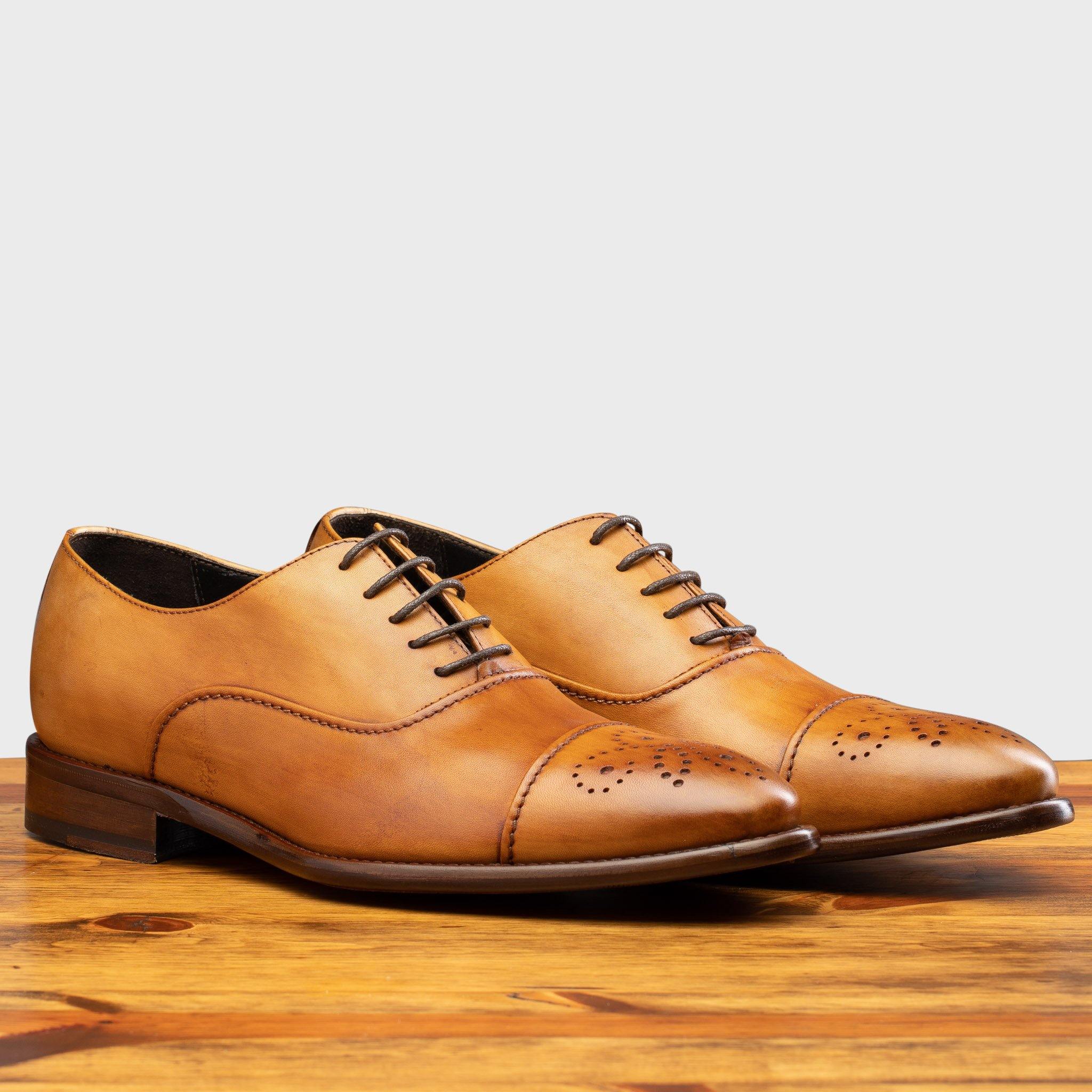 Pair of Dark Caramel leather dress shoe on a wooden surface with a white background