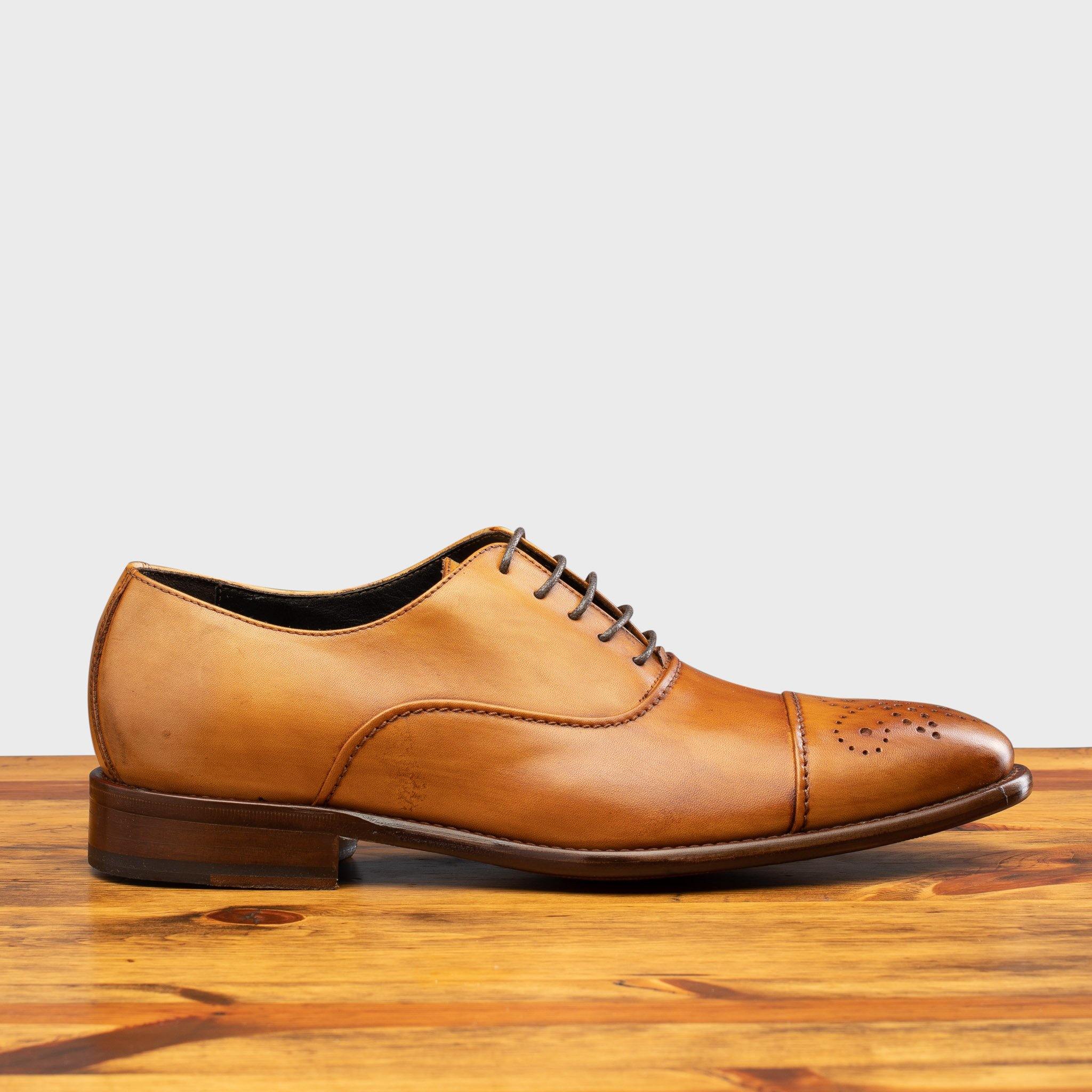 Dark Caramel leather dress shoe on a wooden surface with a white background