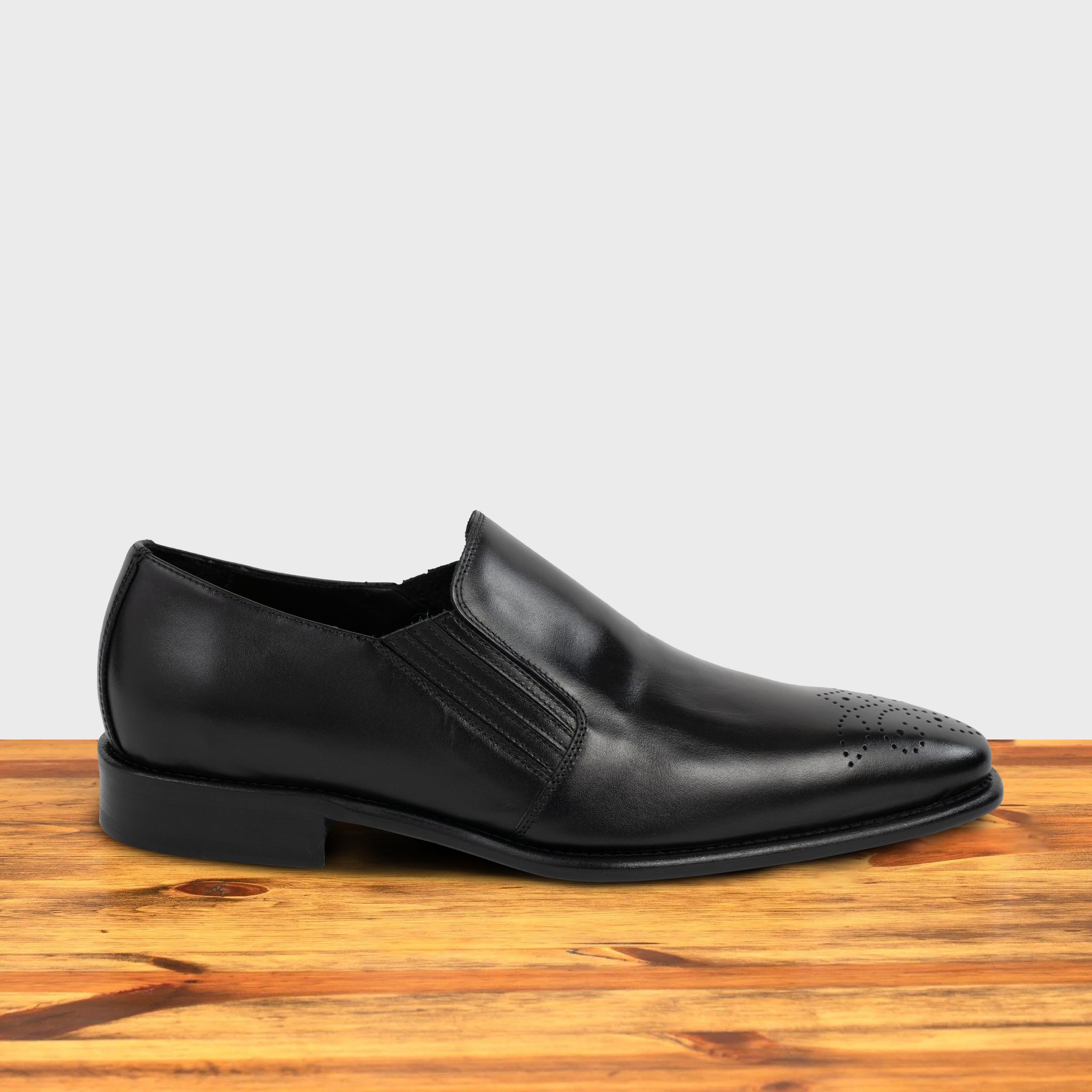 Black leather shoe on a wooden surface with a light gray background