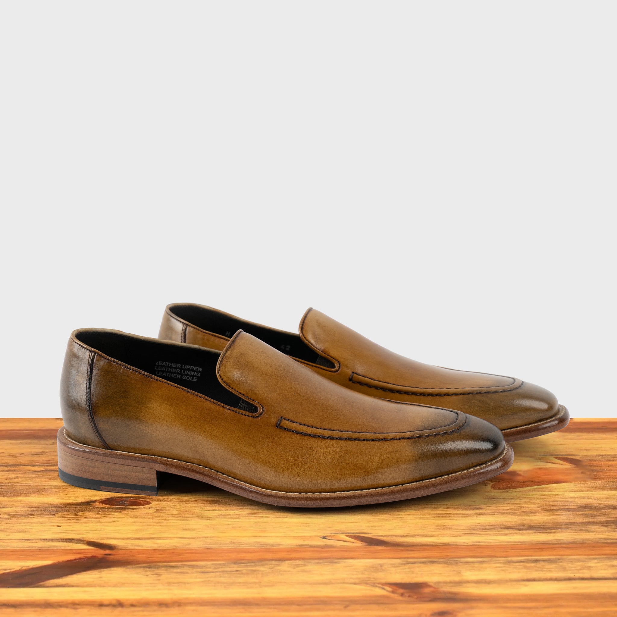 A Pair of Spice leather loafer on a wooden surface with a light gray background