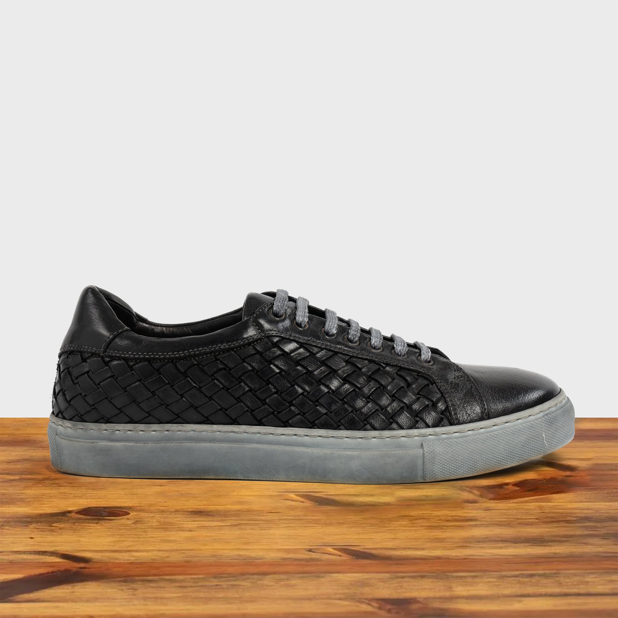 Black woven sneaker on a wooden surface with a light gray background