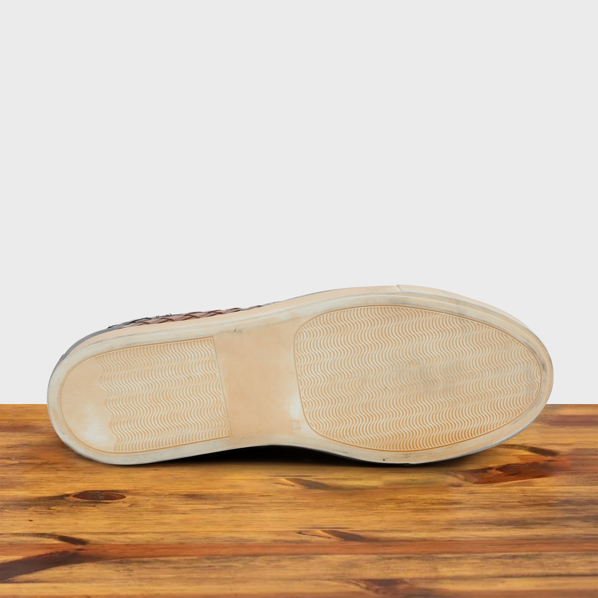 Outsole of Brick woven sneaker on a wooden surface with a light gray background