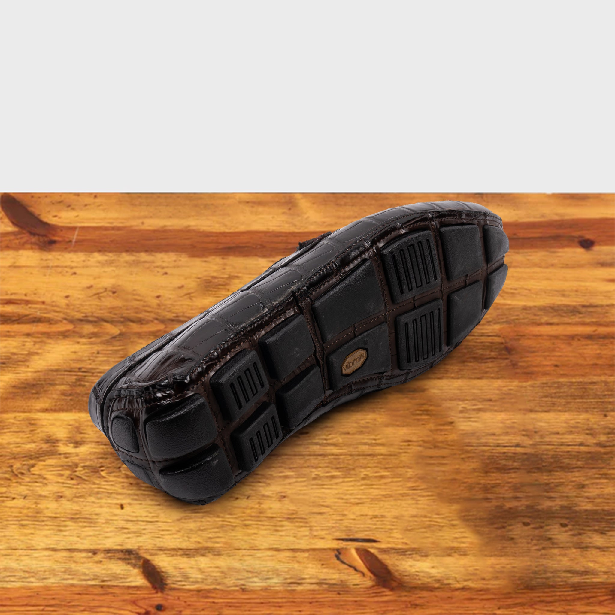 Outsole of Dark Brown crocodile-patterned loafer on a wooden surface with a light gray background