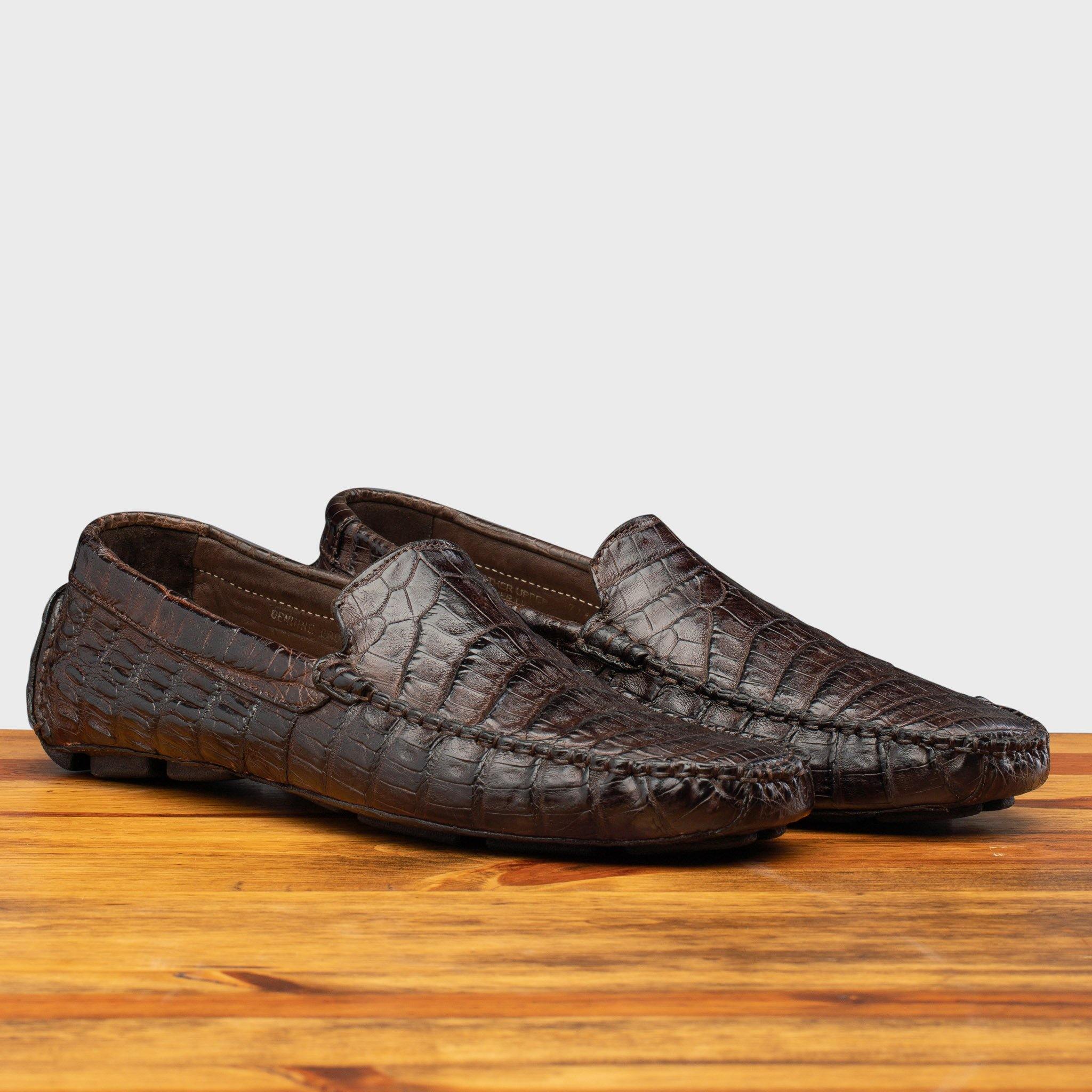 Dark brown crocodile-patterned loafer on a wooden surface with a light gray background