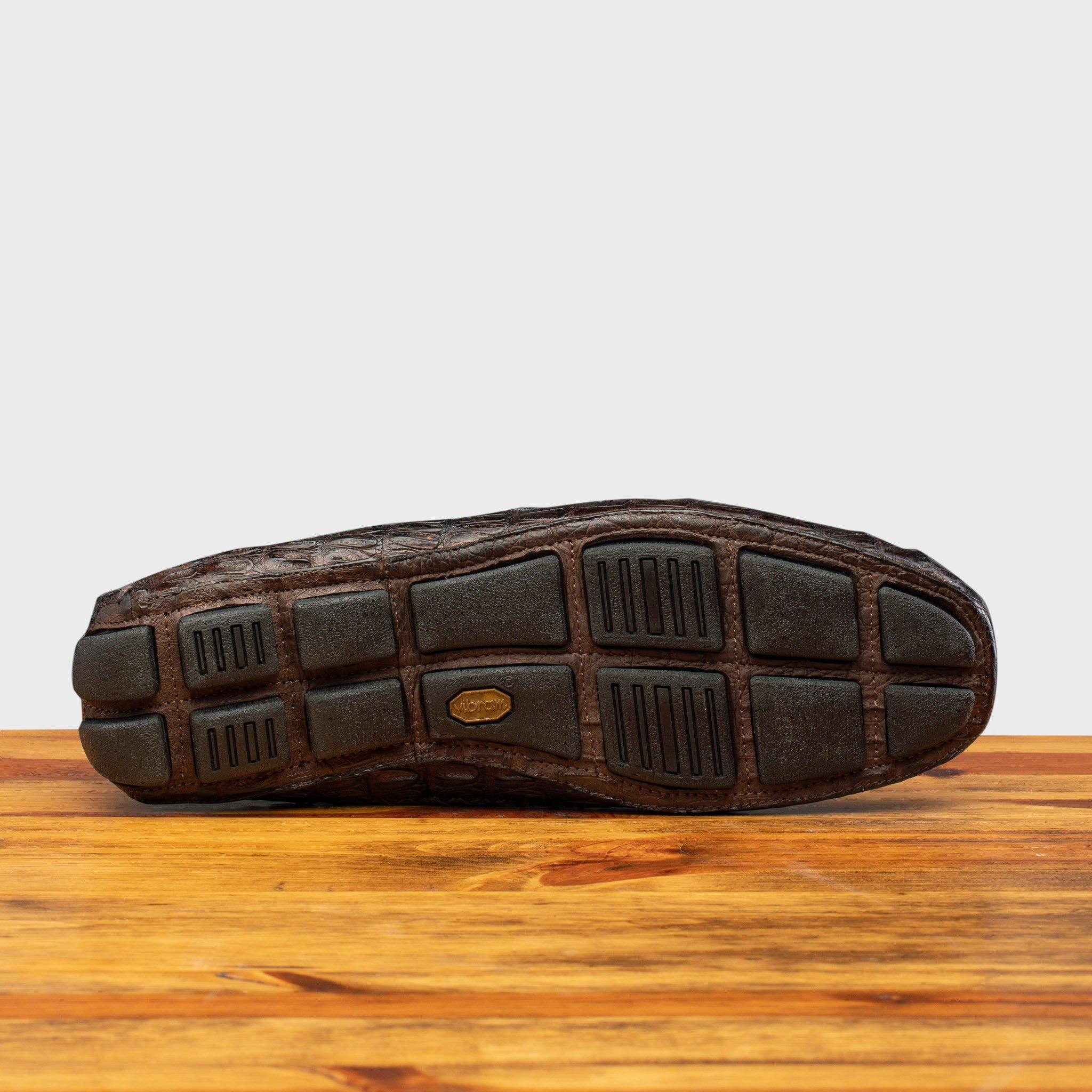 Outsole of Dark brown crocodile-patterned loafer on a wooden surface with a light gray background