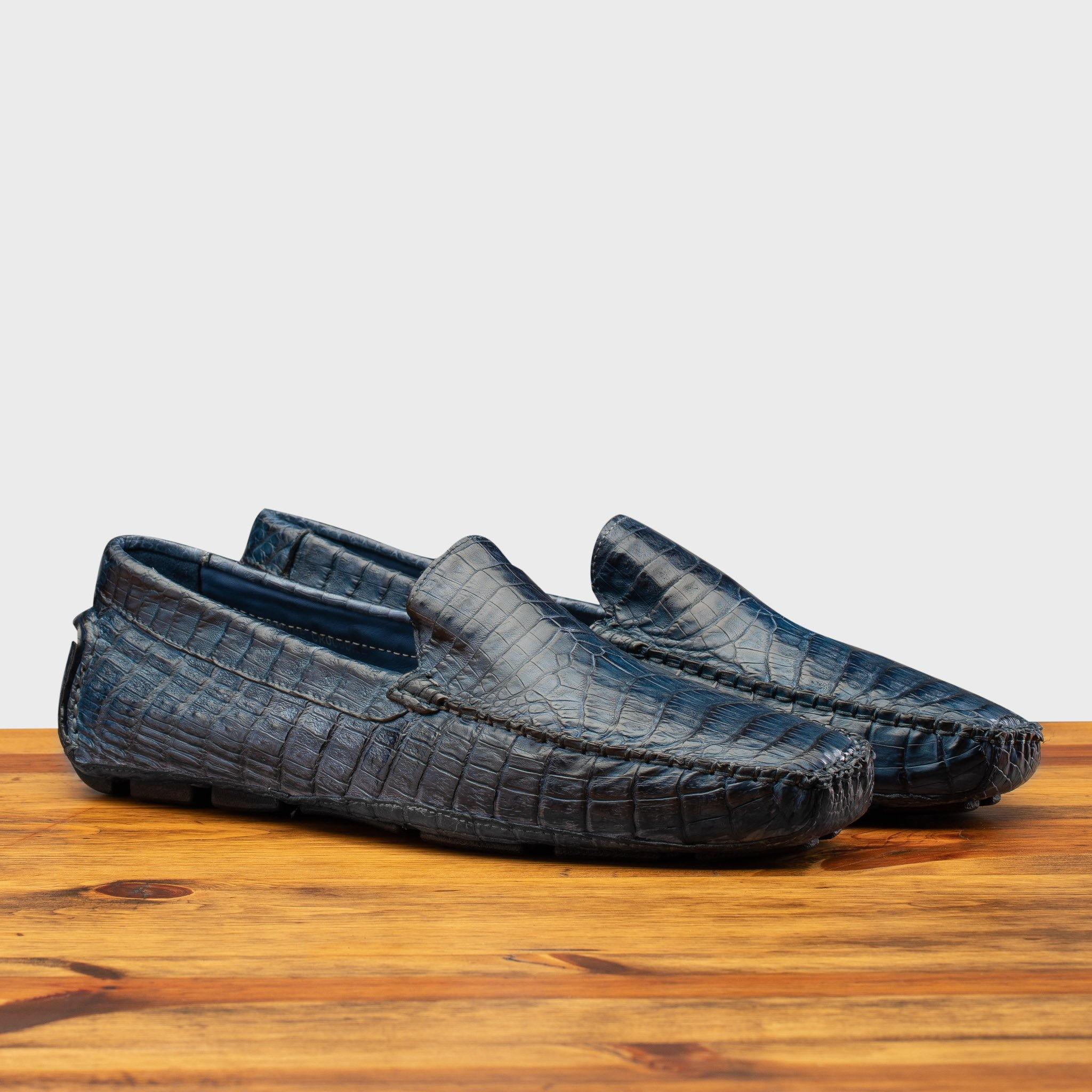 A Pair of Denim crocodile-patterned loafer on a wooden surface with a light gray background