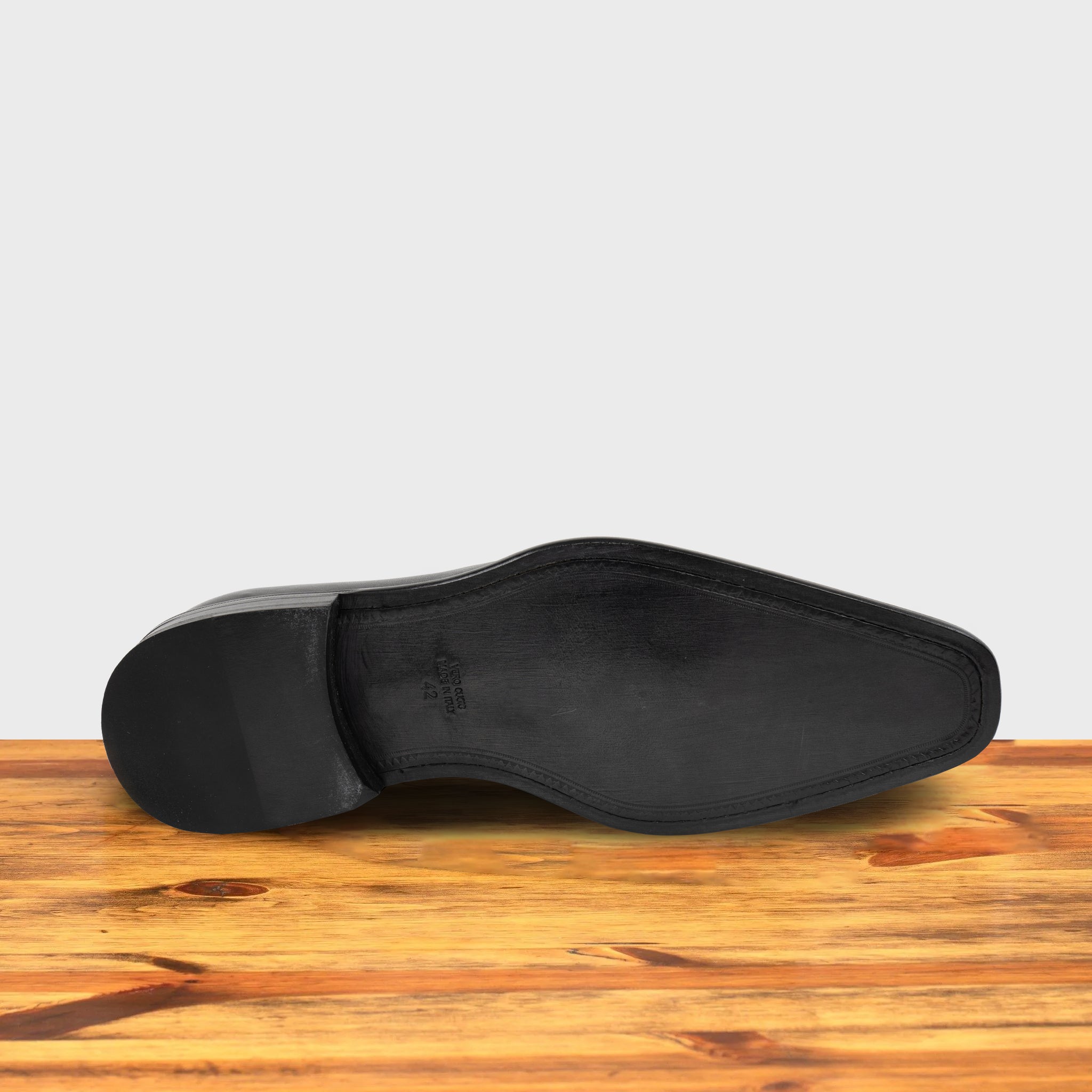 Outsole of Black leather shoe on a wooden surface with a light gray background