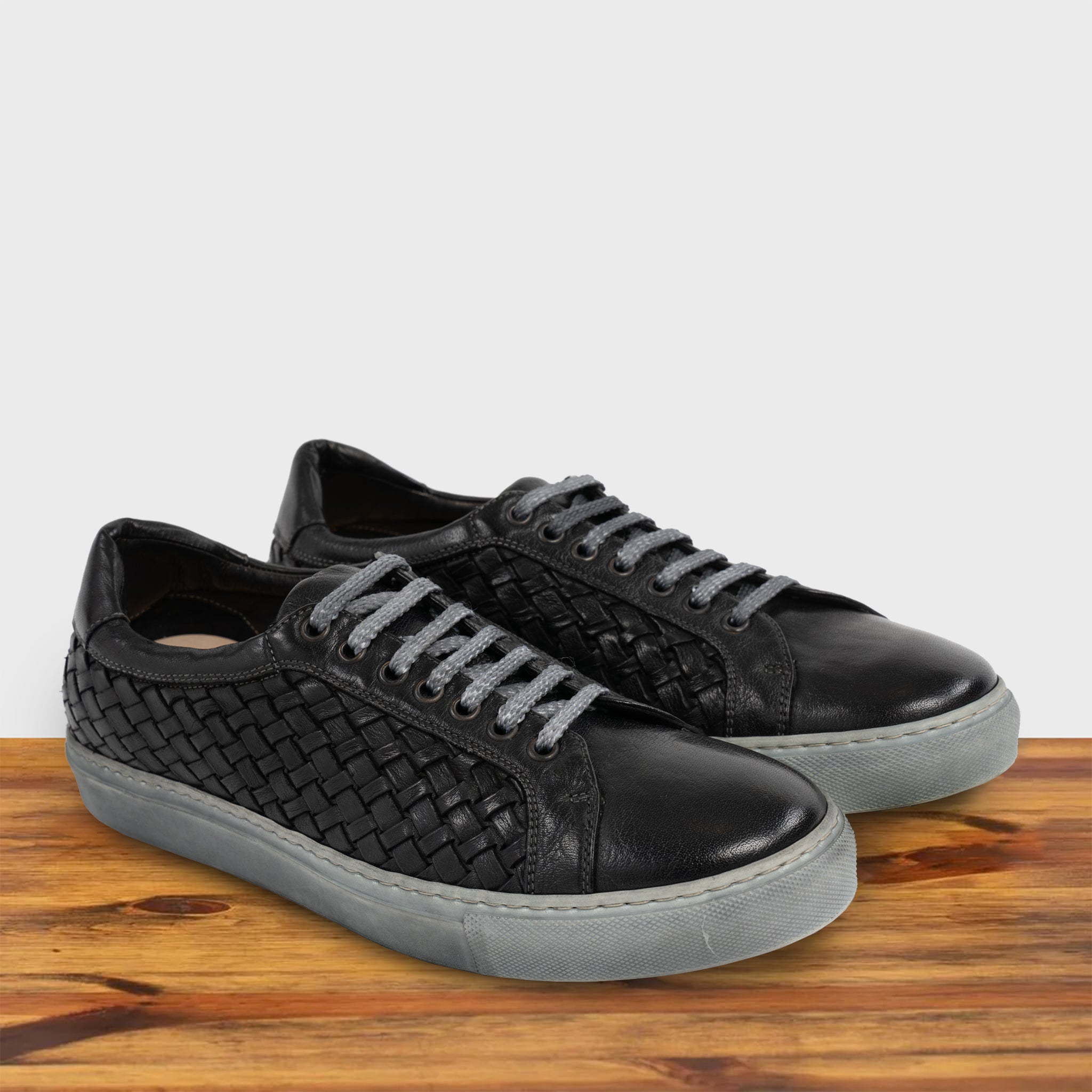 A Pair of Black woven sneaker on a wooden surface with a light gray background