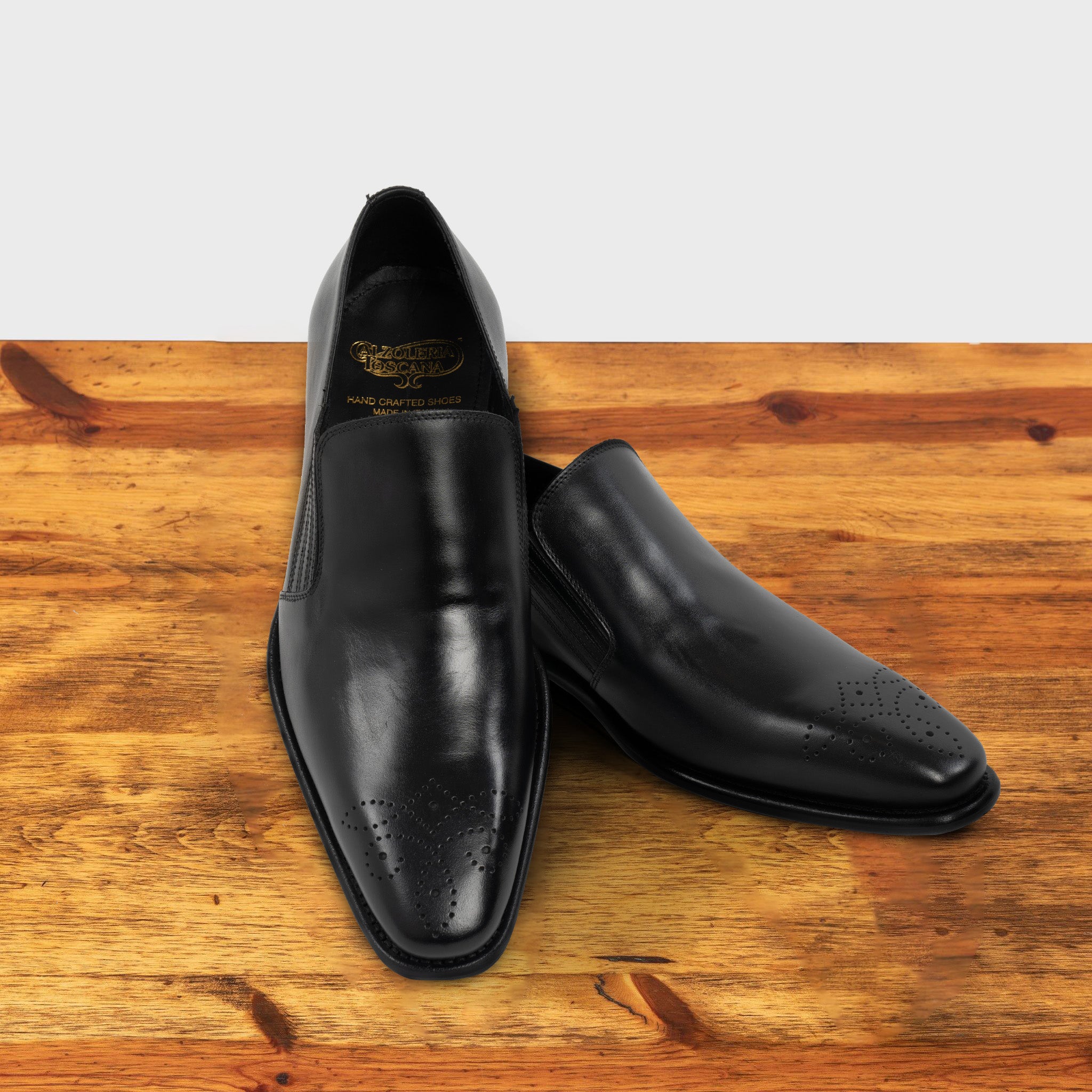 Pair of Black leather shoe on a wooden surface with a light gray background