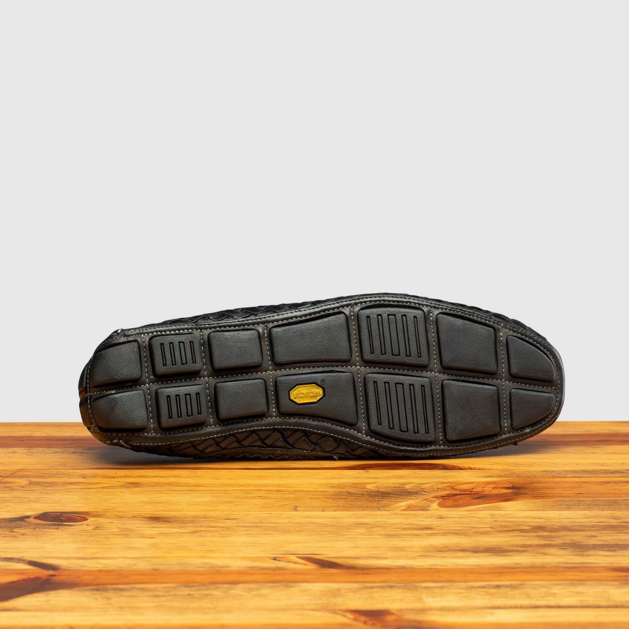 Outsole of Black loafer shoe with woven pattern on a wooden surface