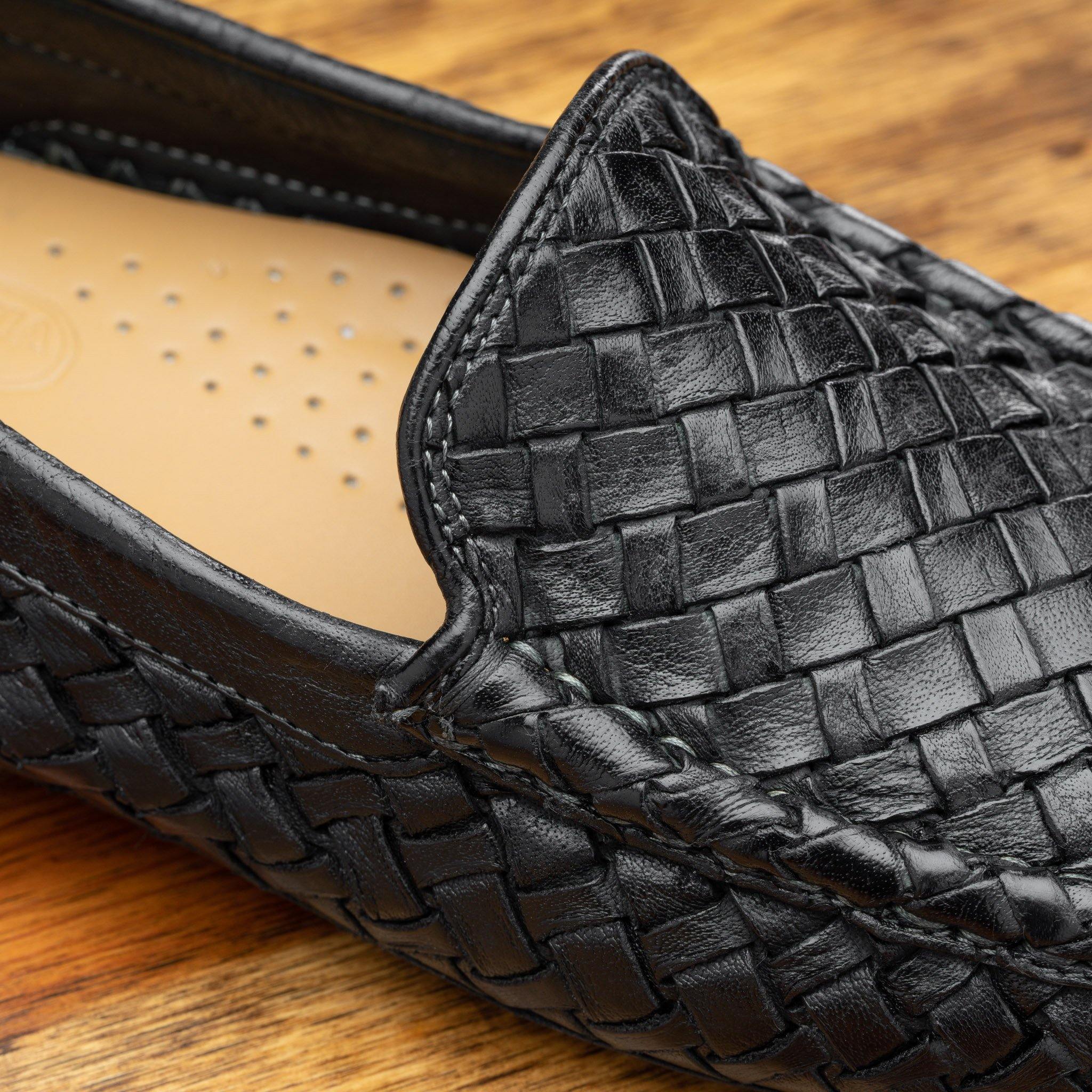 Close-up Black loafer shoe with woven pattern on a wooden surface