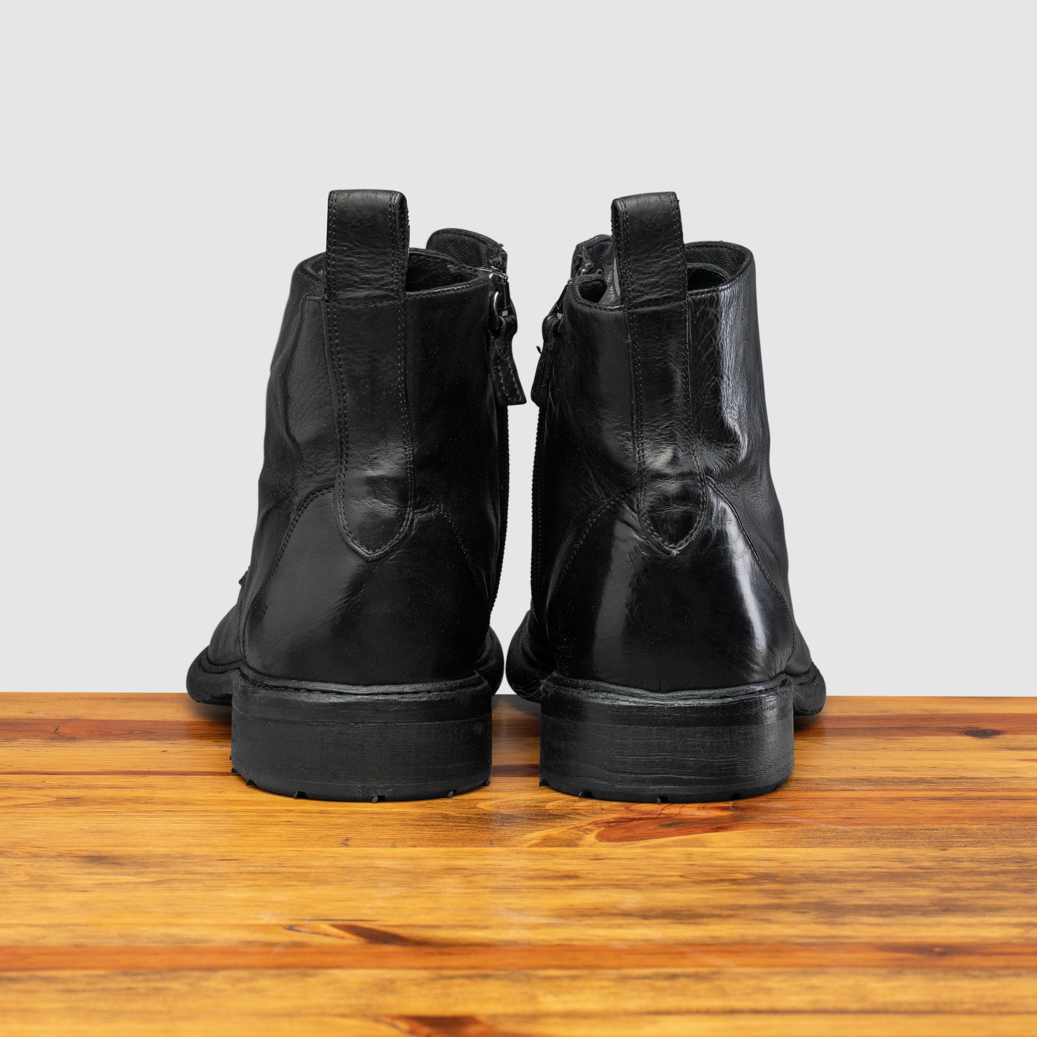 Back view of Black leather boot on a wooden surface with a light gray background