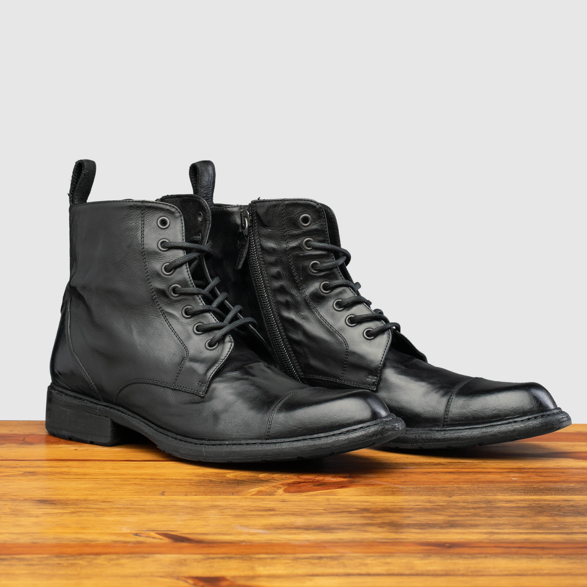 Pair of Black leather boot on a wooden surface with a light gray background