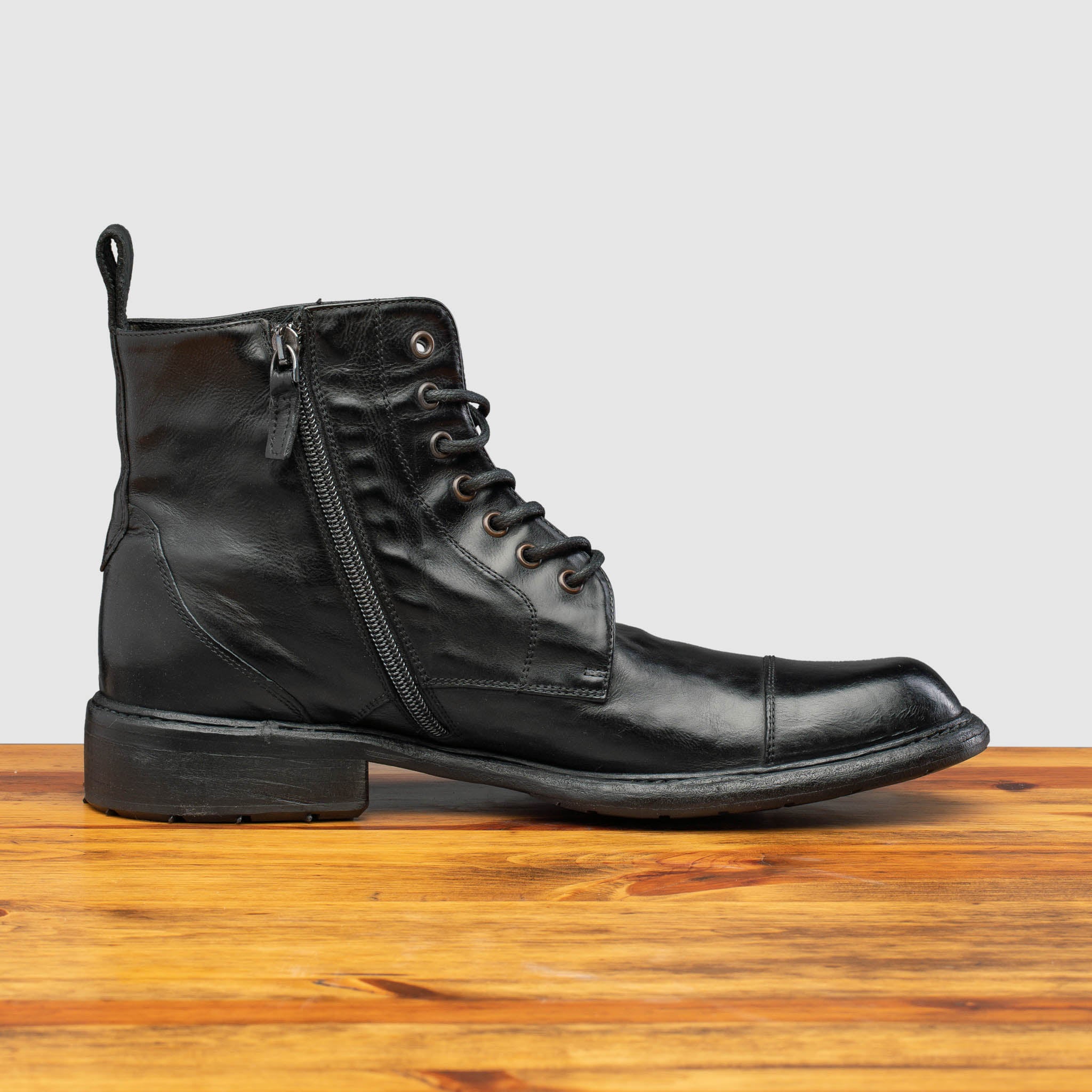 Black leather boot on a wooden surface with a light gray background