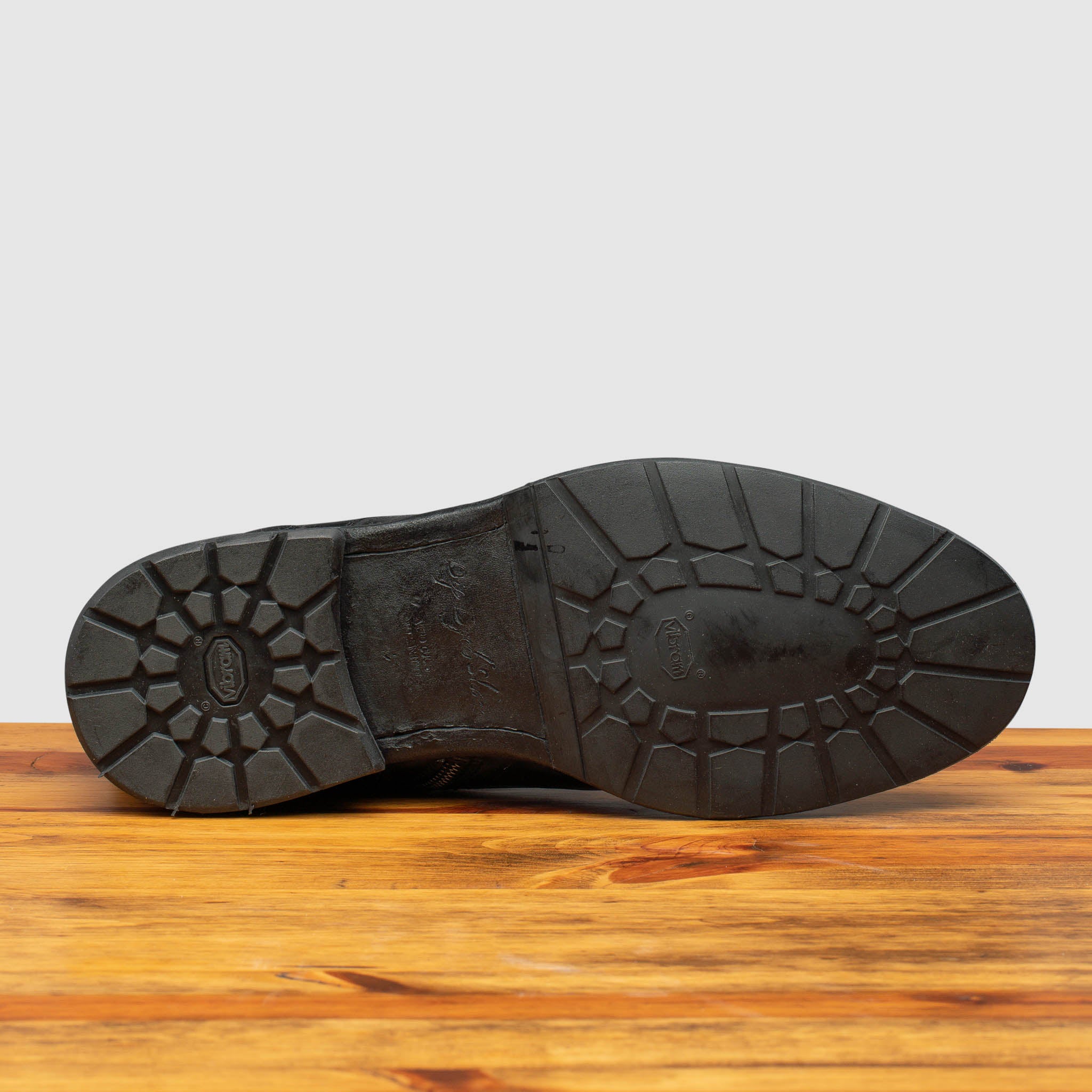 Outsole of Black leather boot on a wooden surface with a light gray background