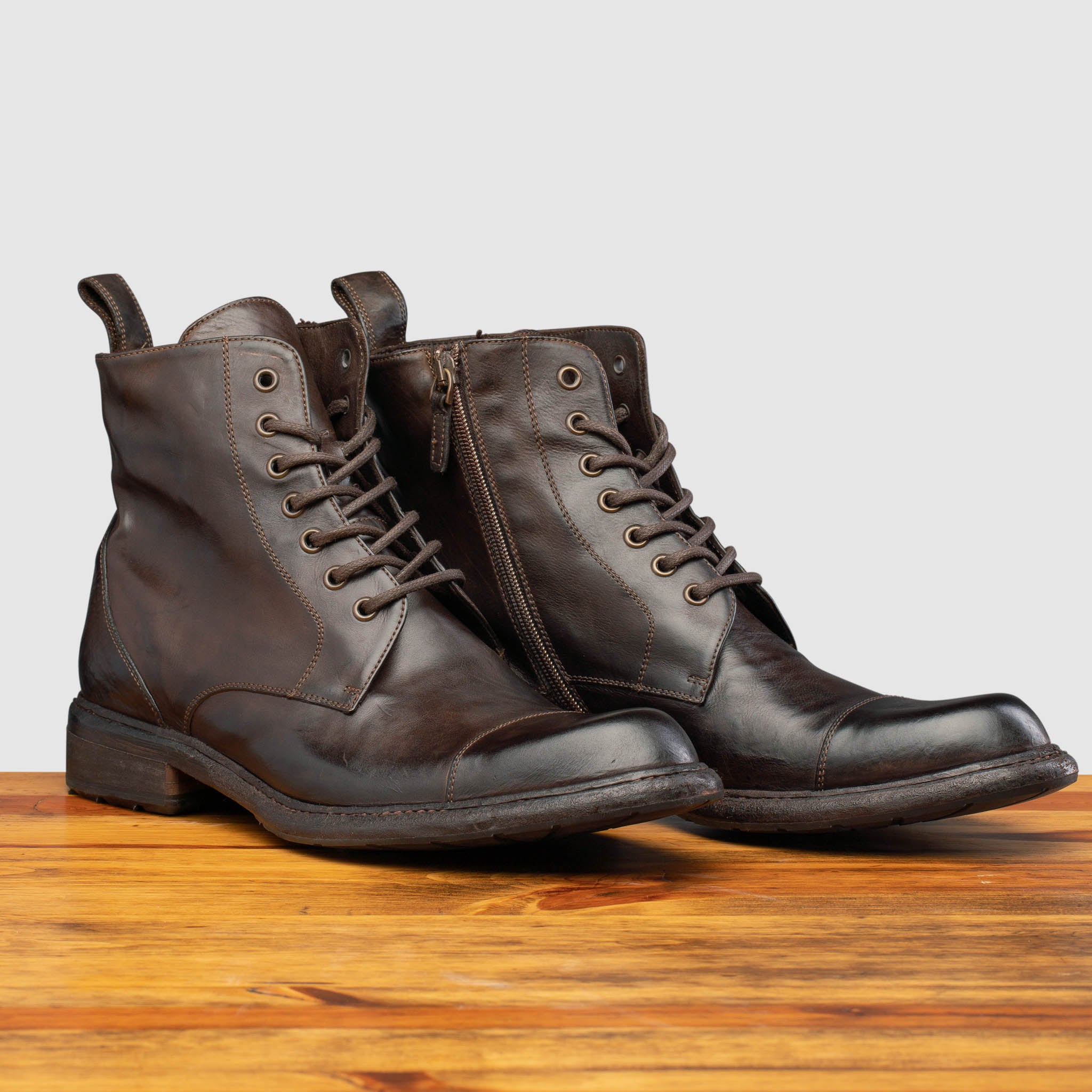 Pair of Brown leather boot on a wooden surface with a light gray background