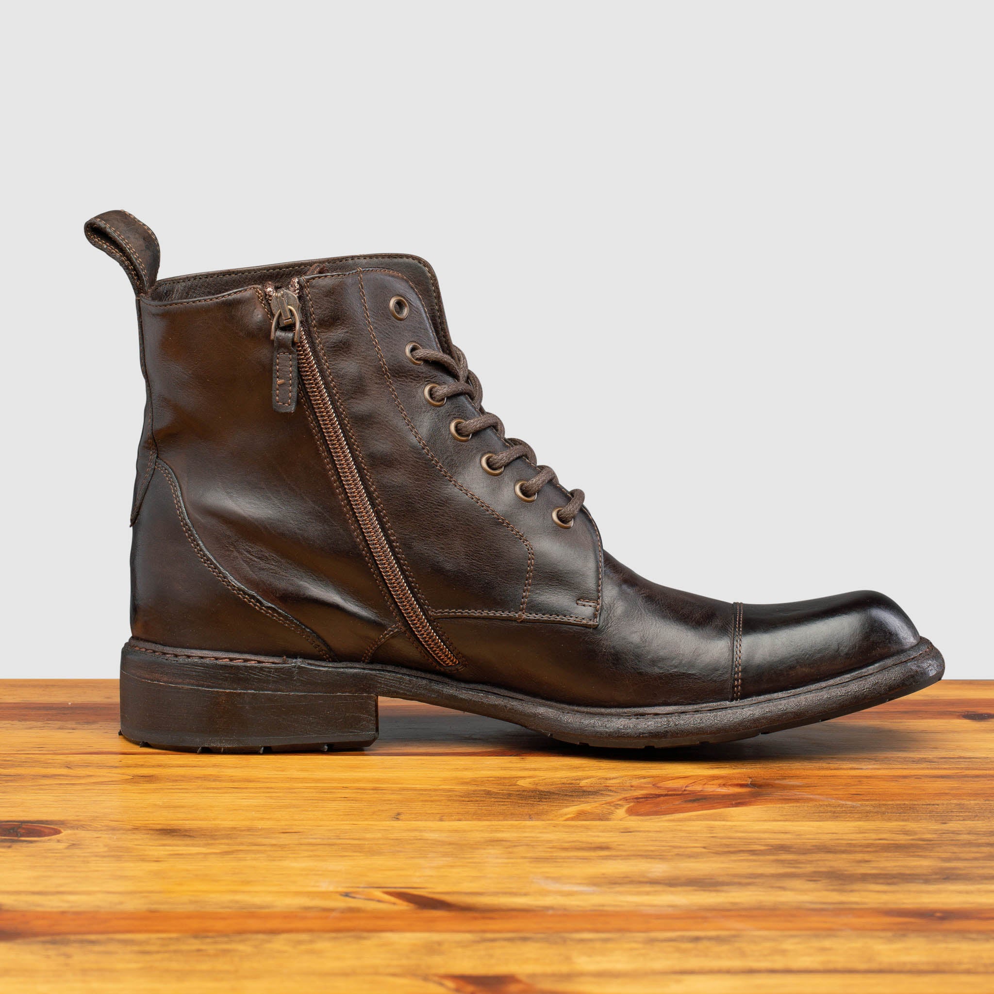 Brown leather boot on a wooden surface with a light gray background