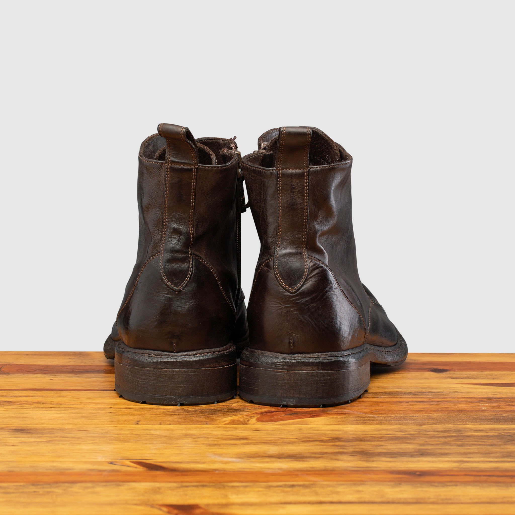 Back view of Brown leather boot on a wooden surface with a light gray background