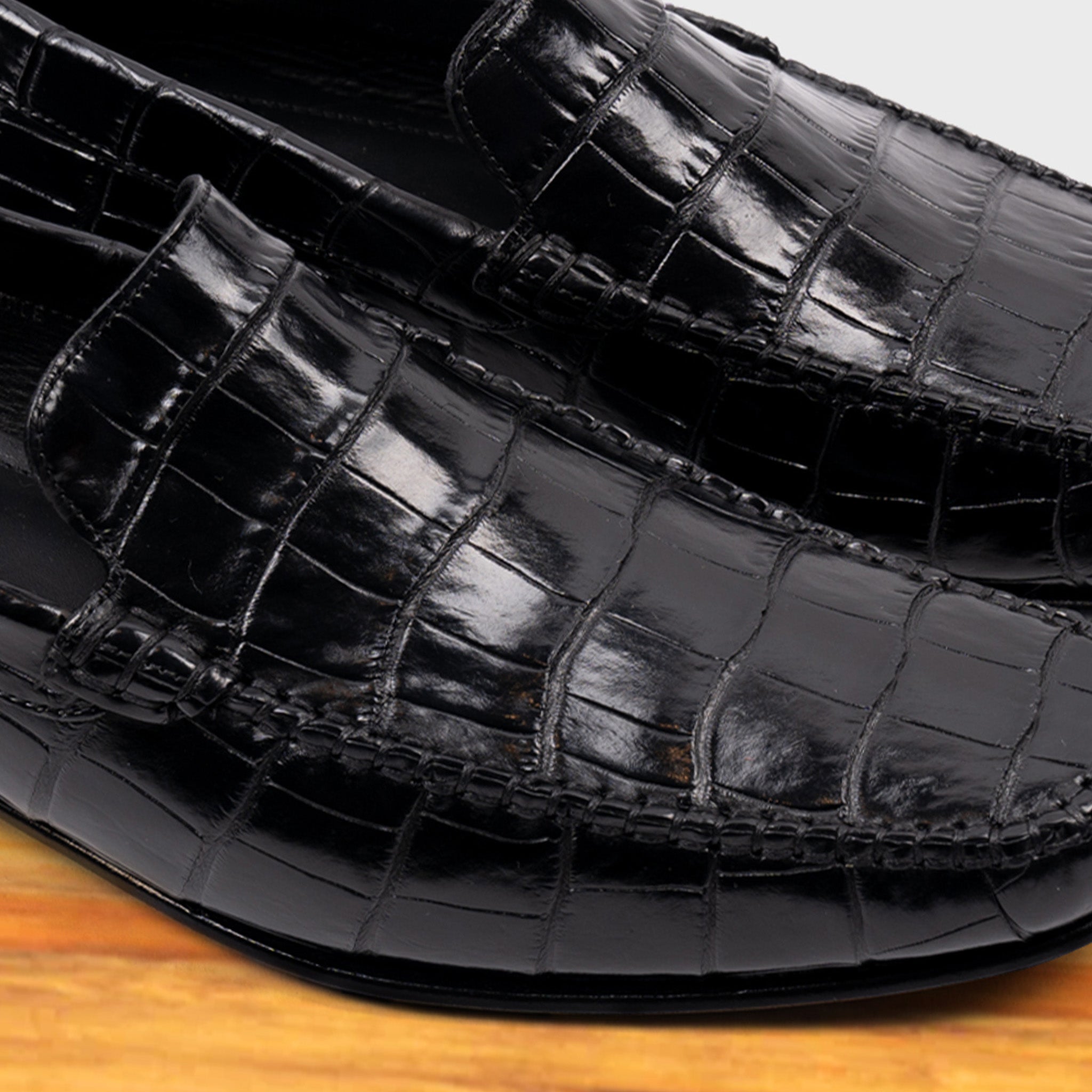 Black crocodile-patterned loafer on a wooden surface