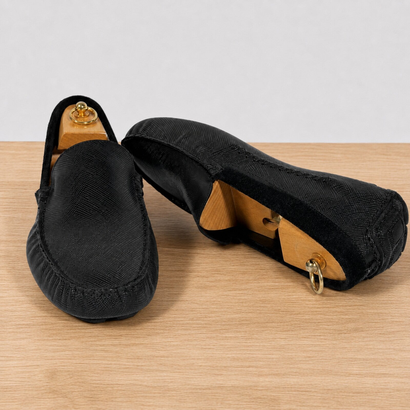 A pair of black slip-on loafers with a textured woven upper, displayed on a light wood surface against a white background.