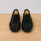 A pair of black slip-on loafers with a textured woven upper, displayed on a light wood surface against a white background.