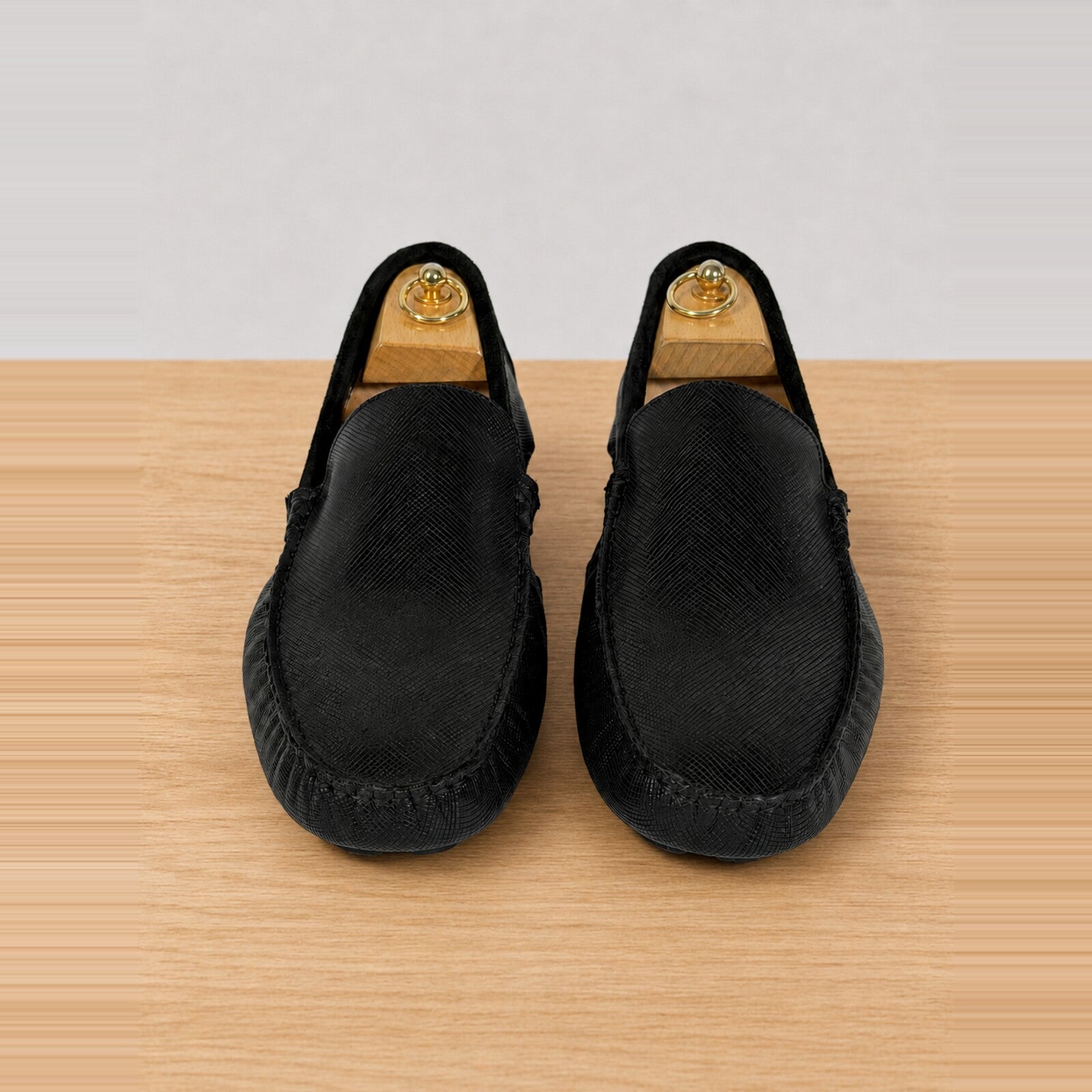 A pair of black slip-on loafers with a textured woven upper, displayed on a light wood surface against a white background.
