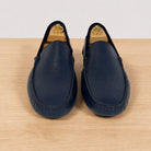 A pair of  blue leather driving loafers with a pebbled texture, displayed on a light wood surface against a neutral light gray background.