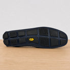 The outsole of a blue shoe resting on a light wood surface against a white background. The sole features a black tread pattern with a small yellow Vibram logo in the center.