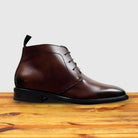 Brown leather boot on a wooden surface with a light gray background