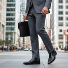 Person in a gray suit holding a black briefcase on a city street wearing black shoes